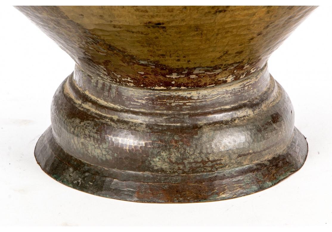 A large and impressive hammered copper circular urn with heavy ring handles and fine elemental form with fine mottled age patina. On a tiered base.
Measures: Height 14 1/2