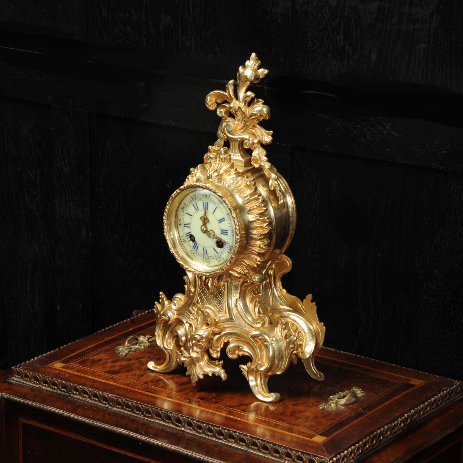A lovely original antique French Rococo boudoir clock, circa 1880. Modelled in gilt brass and typically bold, waisted design with laurel leaves, 'C' scrolls and floral swags. There is a large and elaborate acanthus finial to the top of the case. The