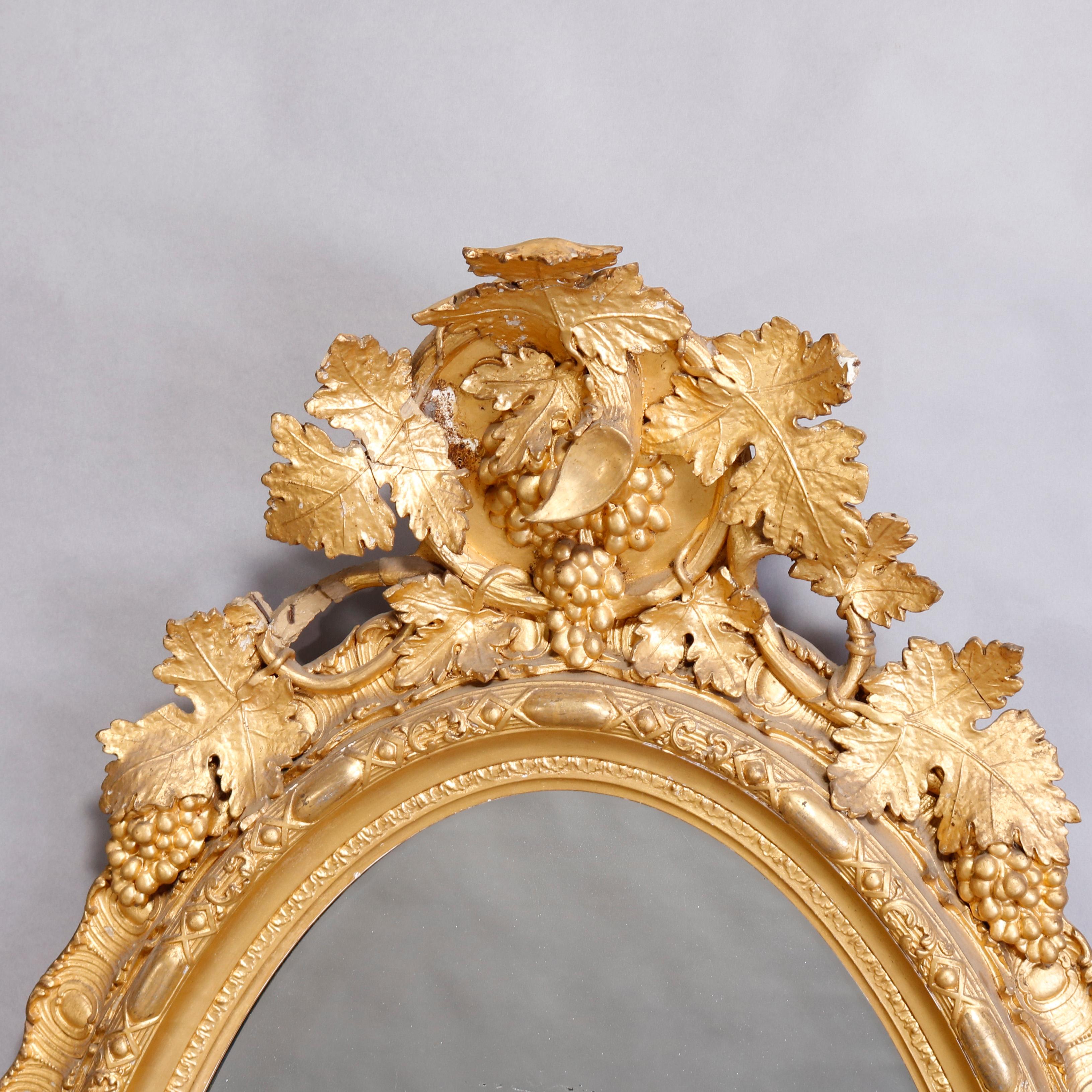 An antique and large French Rococo wall mirror offers oval form with carved giltwood frame having foliate grape and leaf elements, circa 1880.

Measures: 64.5