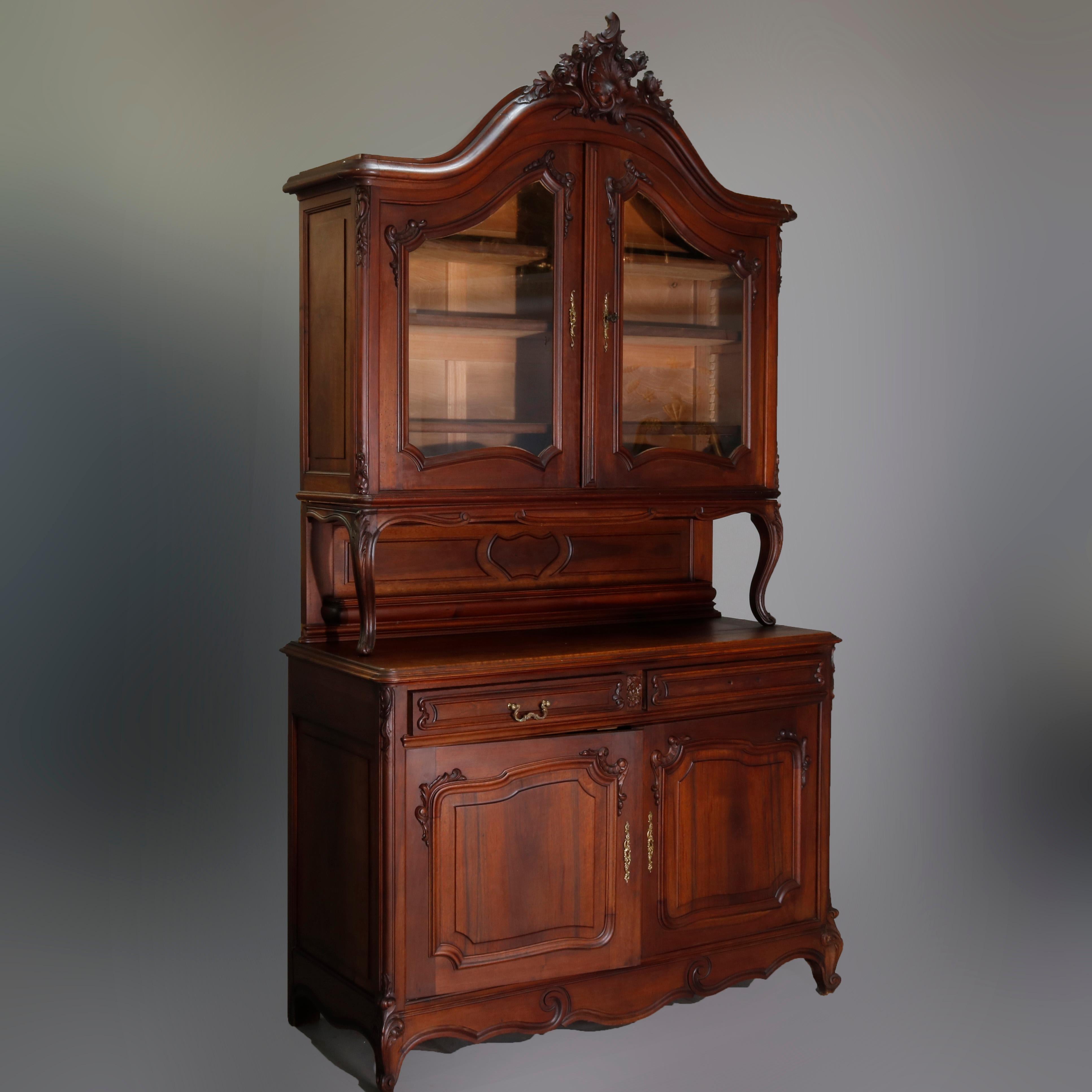 Antique French Rococo carved walnut step back hunt cupboard with arched and asymmetrical foliate and shell carved crest with torch flame surmounting double arched glass door upper with scrolled elements over lower with double drawers and raised