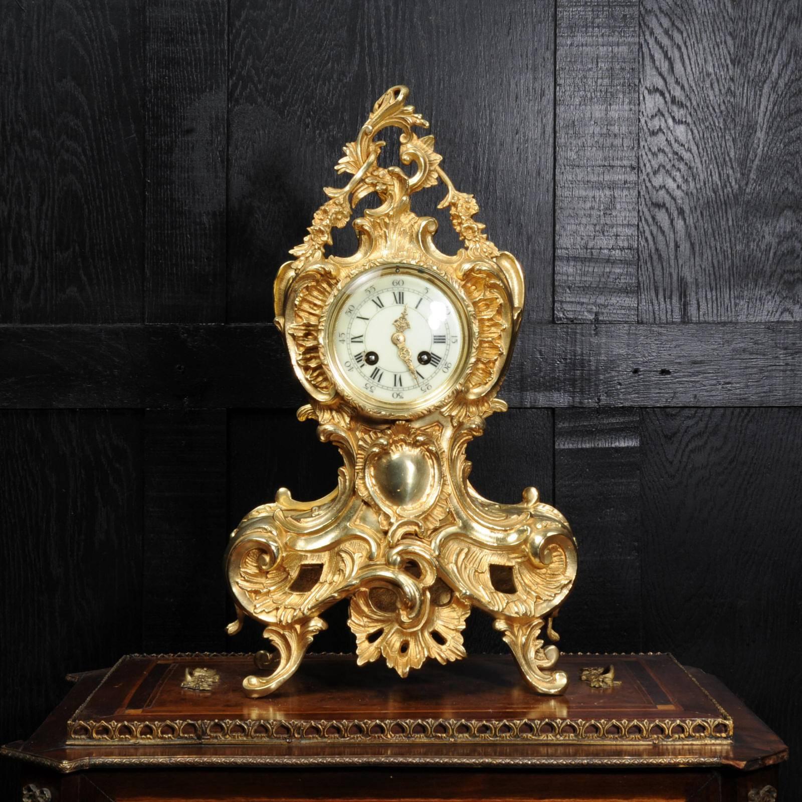 A stunning original antique French gilt bronze Rococo clock. Flamboyant deeply waisted asymmetric Rococo shape decorated with acanthus, scrolls and floral swags. The dial is cream porcelain enamel on copper with separate minute ring and beautifully