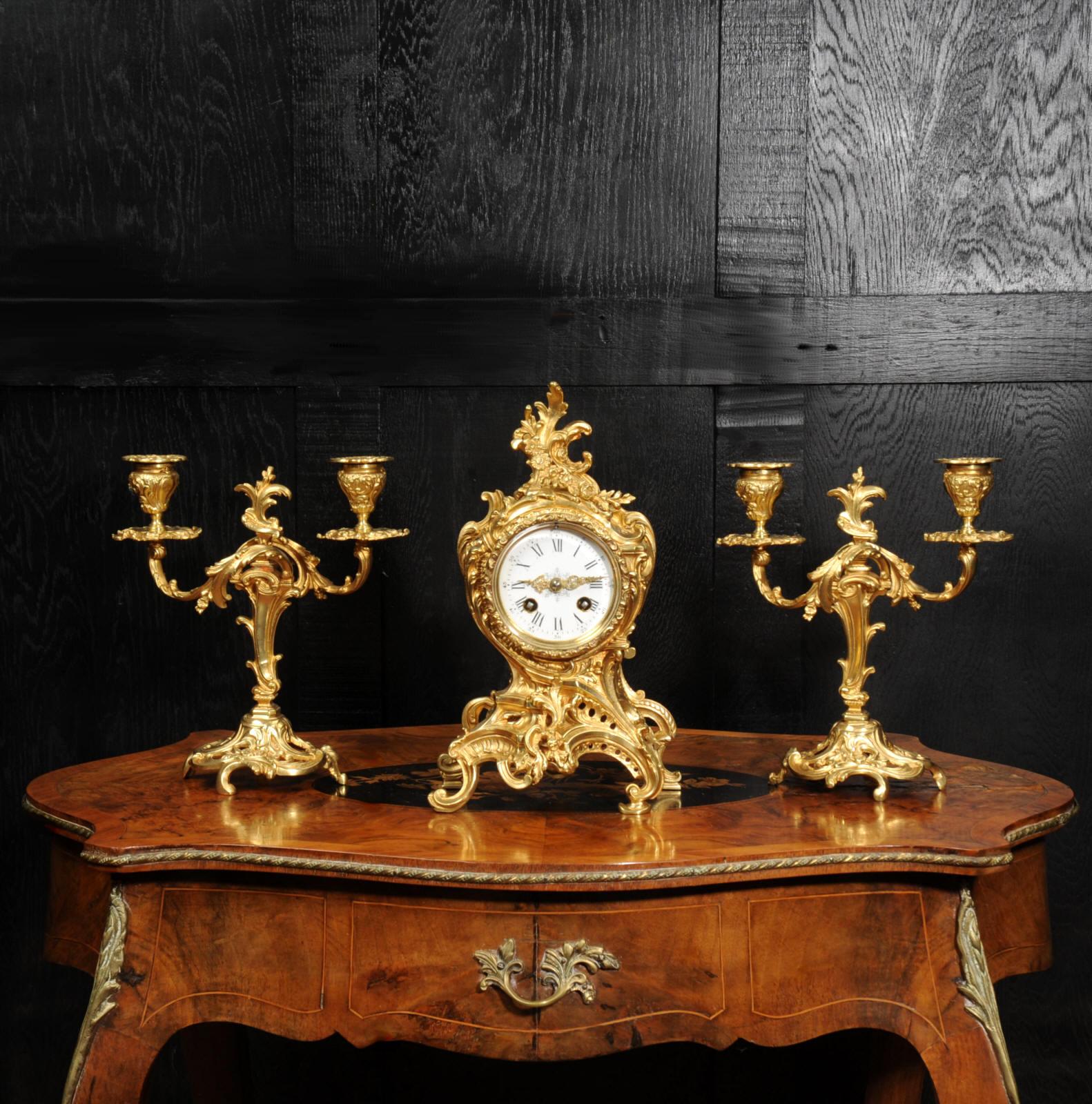 A beautiful original antique French Rococo clock set by Louis Japy. Finely modelled in gilt bronze with a waisted case, formed of asymmetric scrolls with floral swags and a Rococo flourish to the top. Candelabra are conforming in style and have