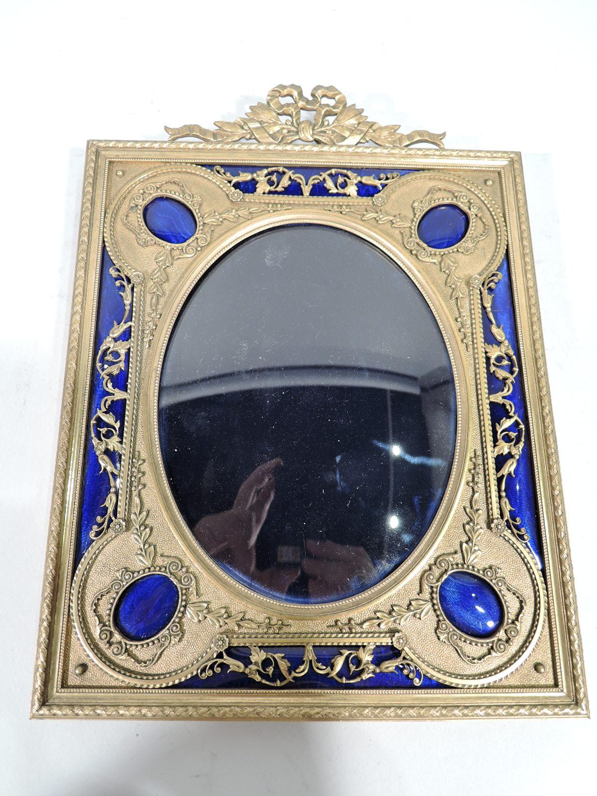 French Rococo gilt bronze and enamel picture frame. Oval window with four open lobes and filigree scrollwork on enamel ground. Surround rectangular with bow-tied ribbon crown. Enamel deep blue. With glass, velvet lining, brocade back, and hinged