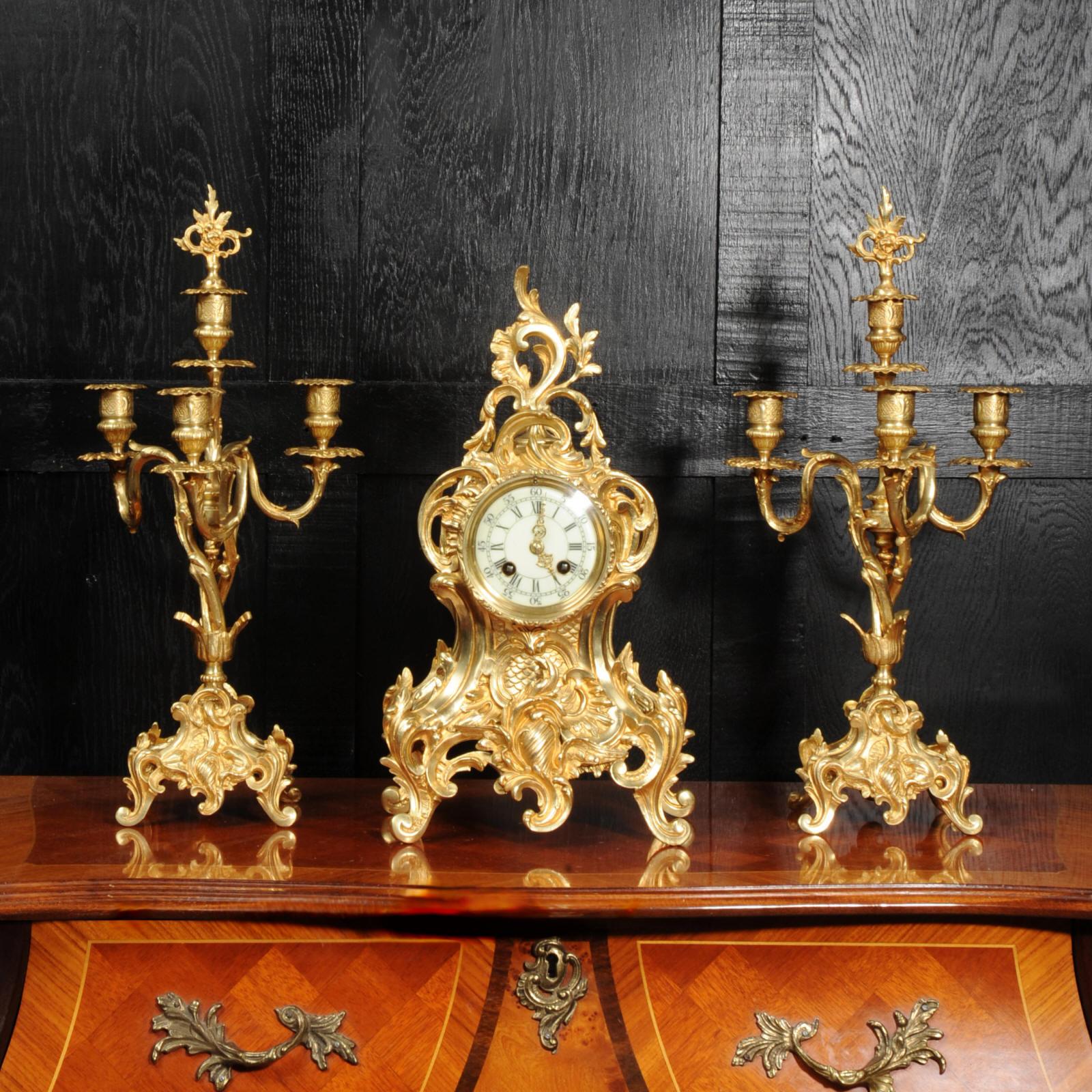 A beautiful original antique French Rococo clock set by Verger Freres of Paris and A. D. Mougin. it is finely modelled with a flamboyantly waisted case covered in C-scrolls and entwined foliage. The candelabra are formed of twirling acanthus