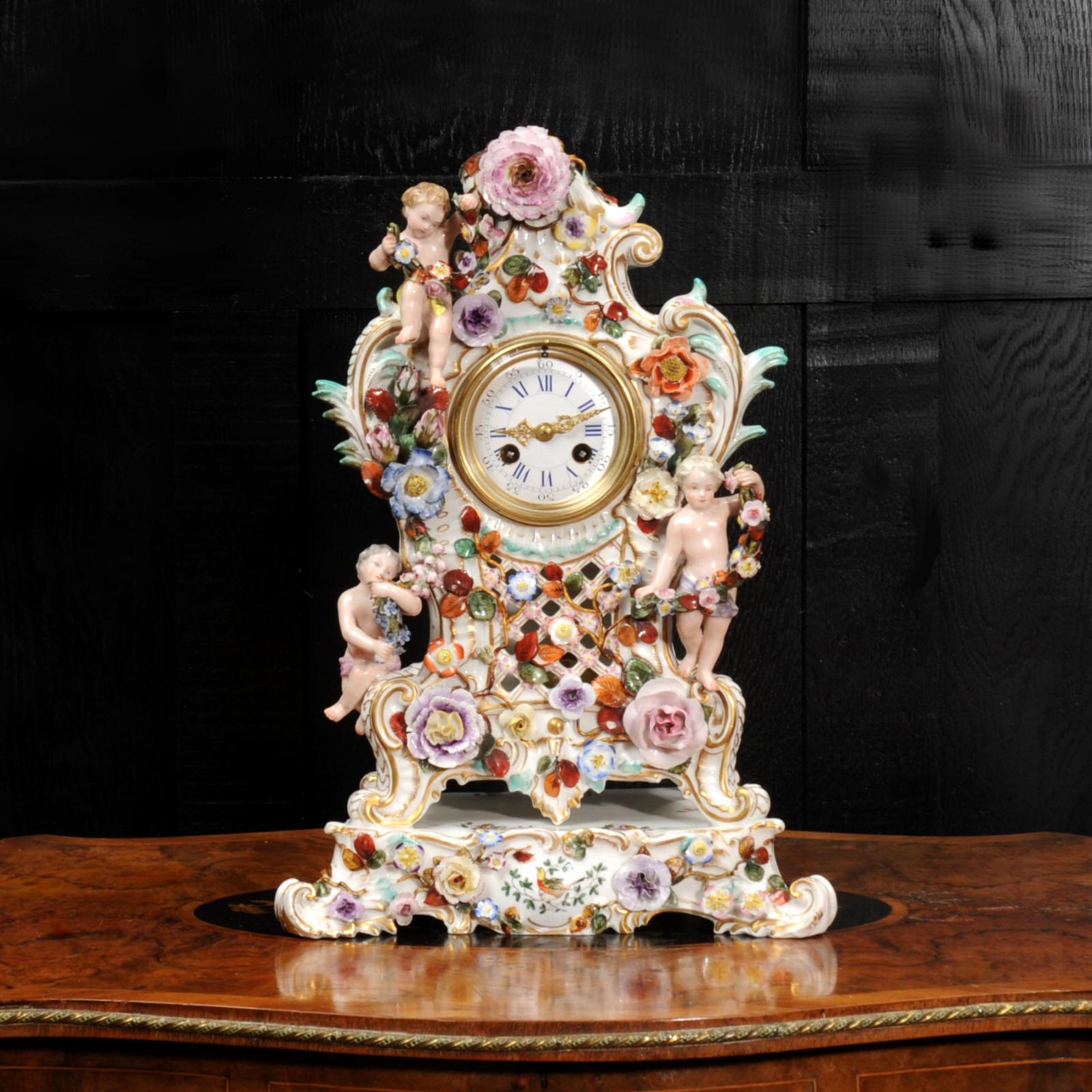 A beautiful antique French clock of exquisite Meissen style porcelain in the Louis XV Rococo style. The case is of waisted shape with bold scrolls sitting upon a base. Three charming putti hold fine floral swags and the case is profusely decorated