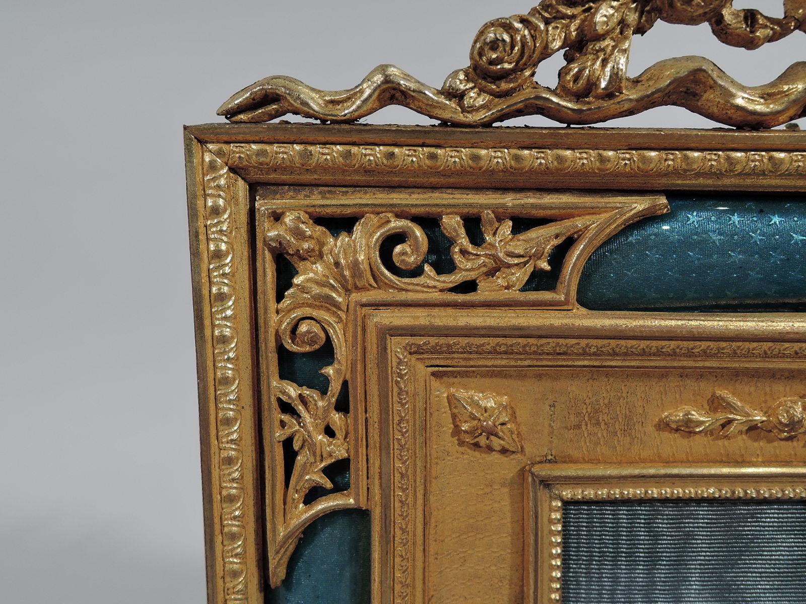 French Rococo Revival gilt bronze and blue enamel picture frame, ca 1900. Rectangular with ribbon-tied floral garland crown. Vertical rectangular window has concave border with applied ribbon-tied garlands and rosettes on wavy ground, in turn