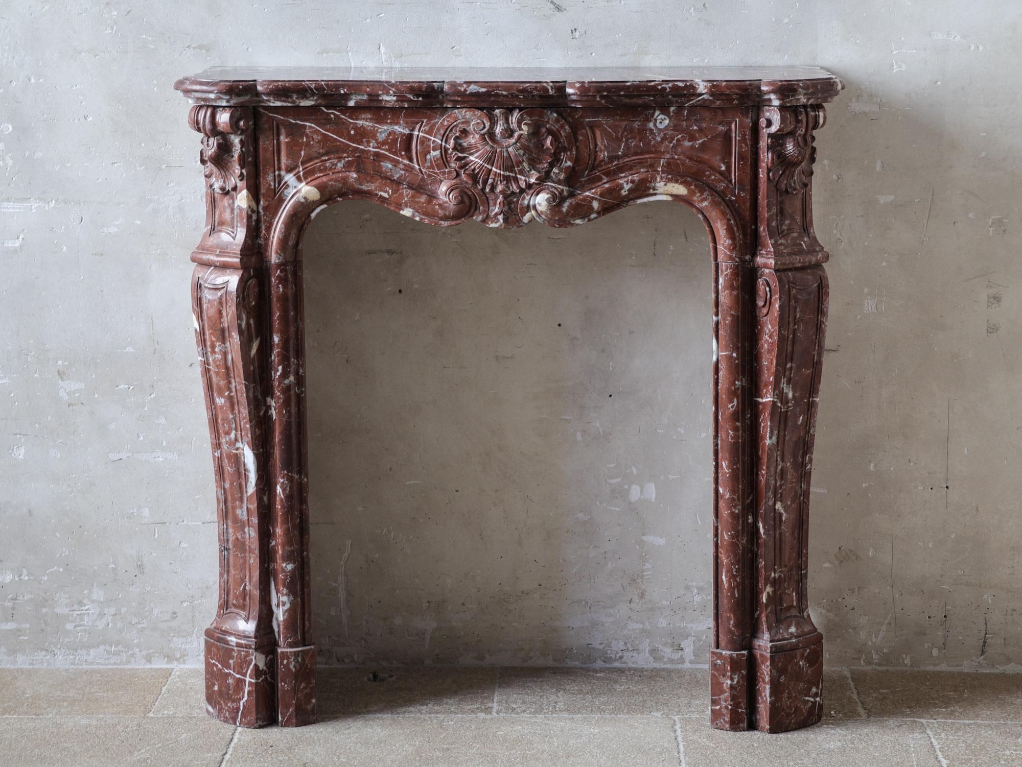 Esta hermosa chimenea antigua es un modelo Trois Coquilles tallado a mano, elaborado con el impresionante mármol Rouge Royal. Esta chimenea de mármol rojo presenta elegantes detalles en gris y blanco, que le añaden profundidad y sofisticación. Con