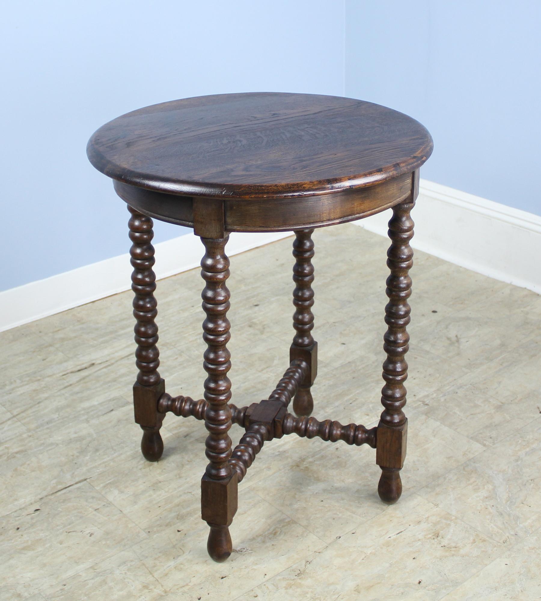 A round bobbin legged side table in rich dark brown oak. Criss-cross stretcher base adds to the look. In excellent sturdy antique condition.