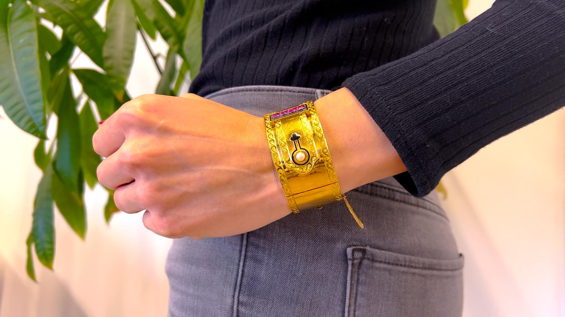 Un bracelet manchette à charnière en or jaune 18k avec rubis et diamants. Une perle, mesurant 4,76 mm. Quatre rubis coussinés de taille mixte, d'un poids total d'environ 1,50 carat, rehaussent l'ensemble. Toutes les pierres précieuses sont classées