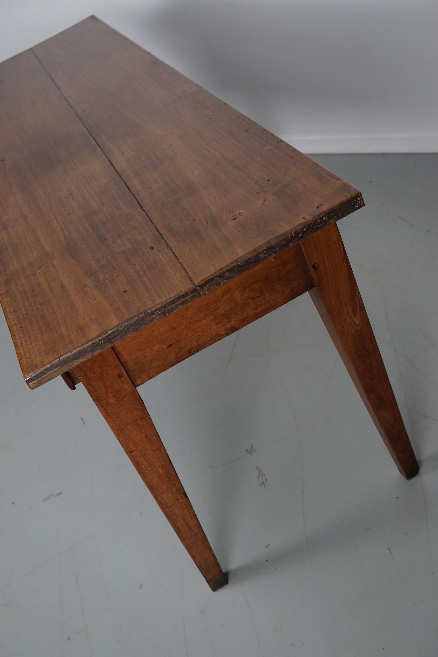Cette élégante table a été fabriquée en France à partir d'une ancienne table à manger en bois de fruitier aux magnifiques veinures. Elle a une couleur chaude avec une brillance profonde et la table montre de nombreuses marques d'utilisation et a une
