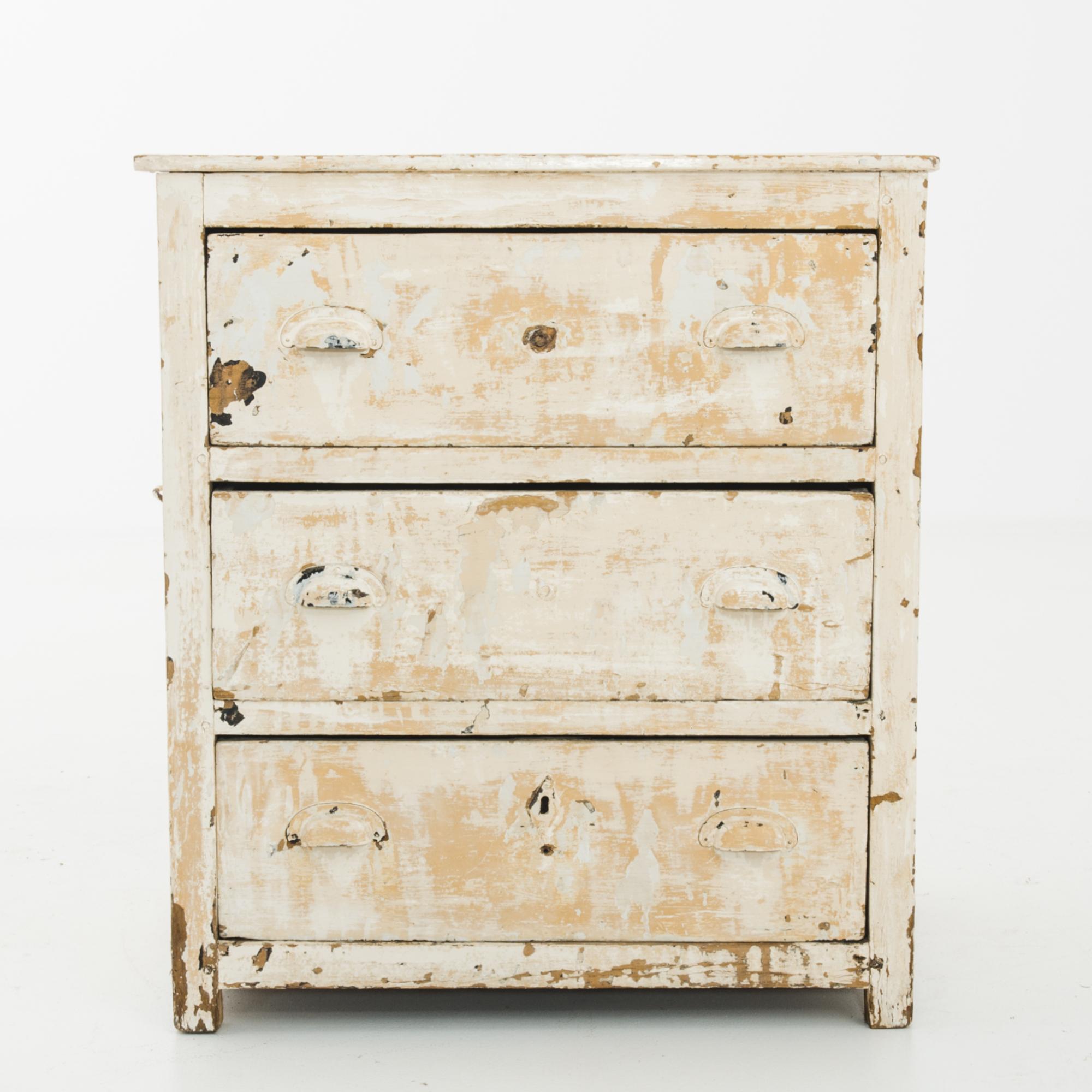 A wooden chest of drawers from France, circa 1900, with a striking patinated finish. The original white paint has weathered with age, revealing a color palette of cream, apricot and natural wood. The deep drawers pull out with cup handles; drop