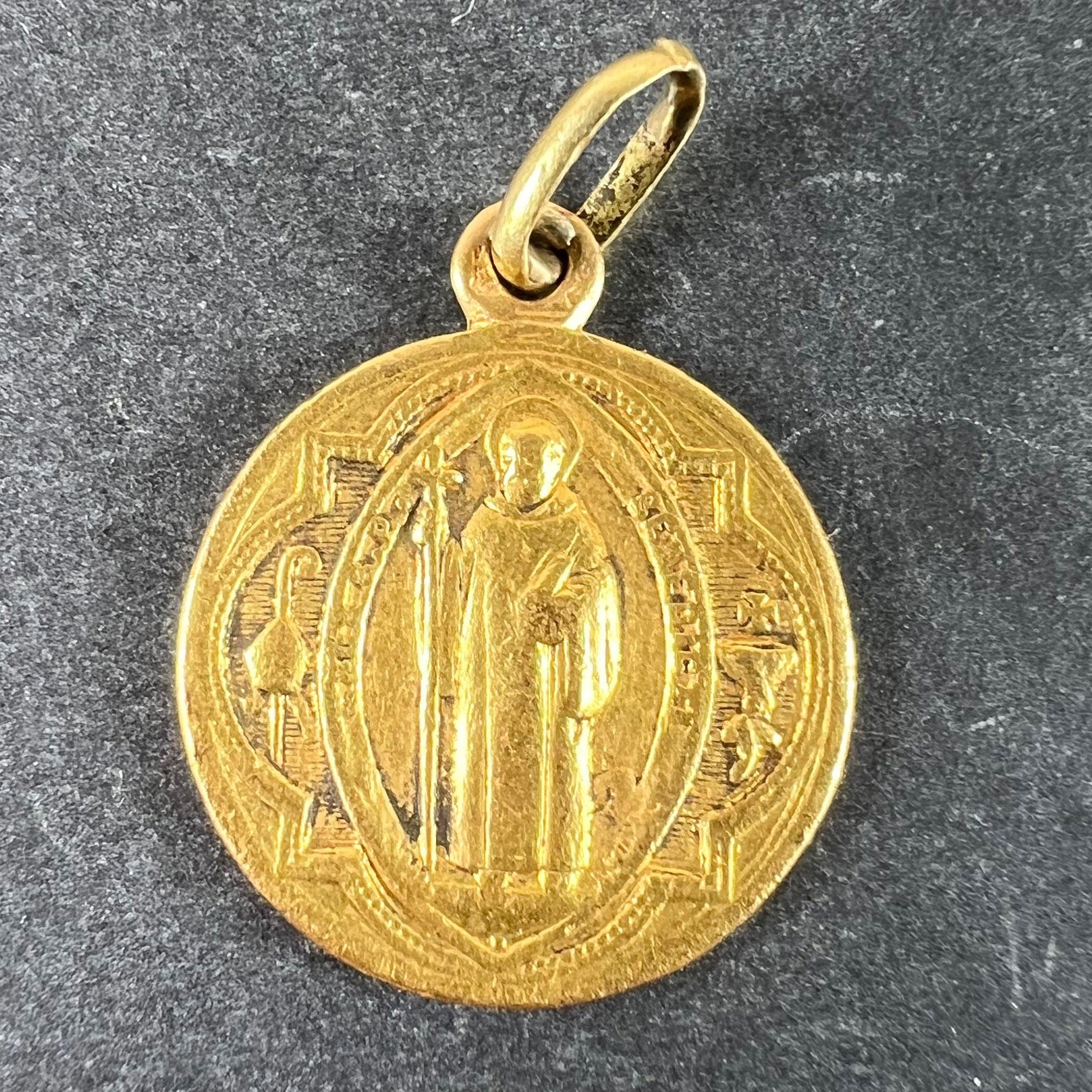 An antique French 18 karat (18K) yellow gold charm pendant designed as a medal depicting Saint Benedict in a gothic frame with the papal mitre and crozier to the left, and a poisoned cup with serpent entwined around the stem and a cross above it to