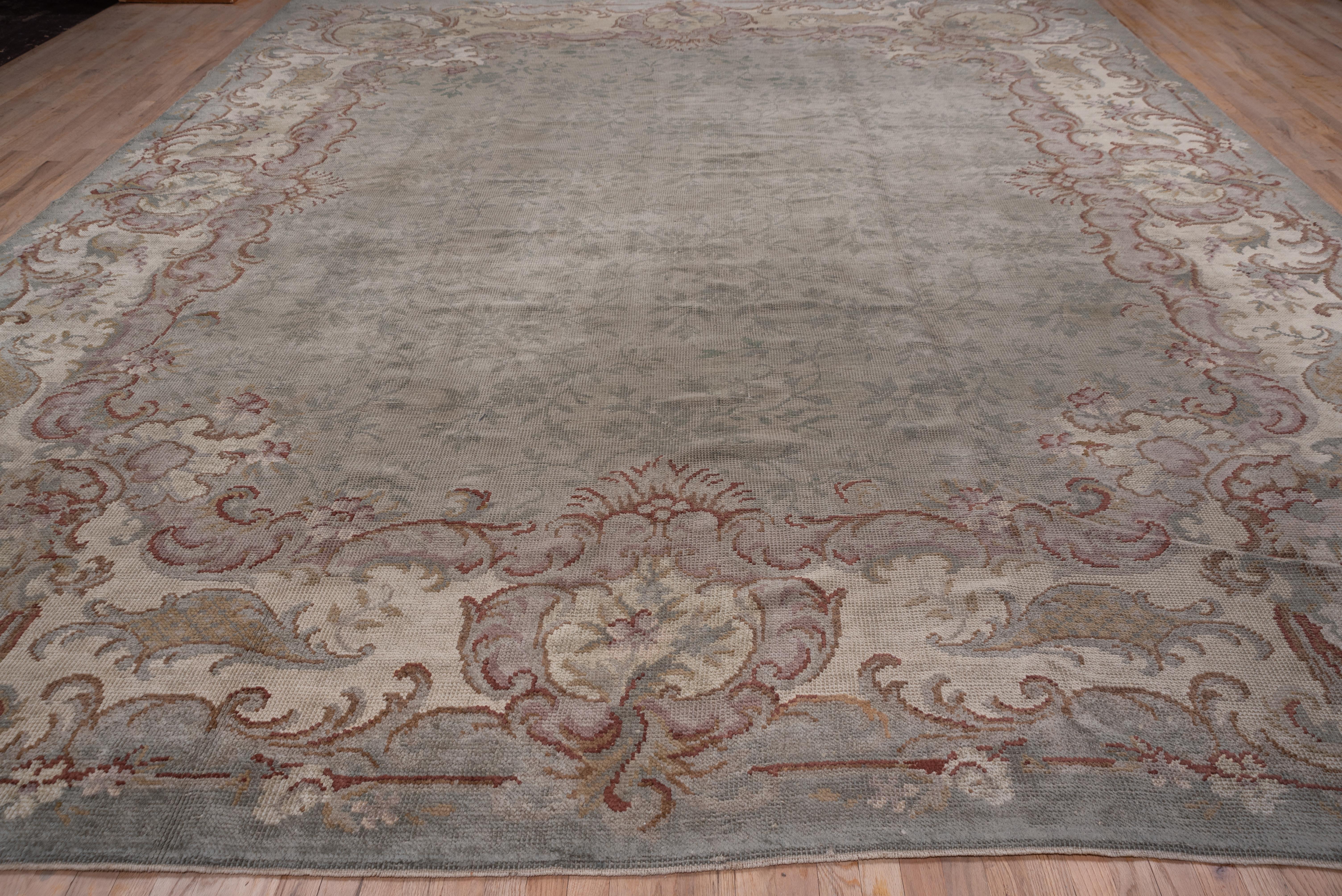This antique French carpet presents a tone-on-tone stem, leaf and flower field pattern within a wide, bold Rococo border of acanthus leaves and scrolls. The light, but not exactly pastel palette includes light green, ivory, beige, reddish brown.