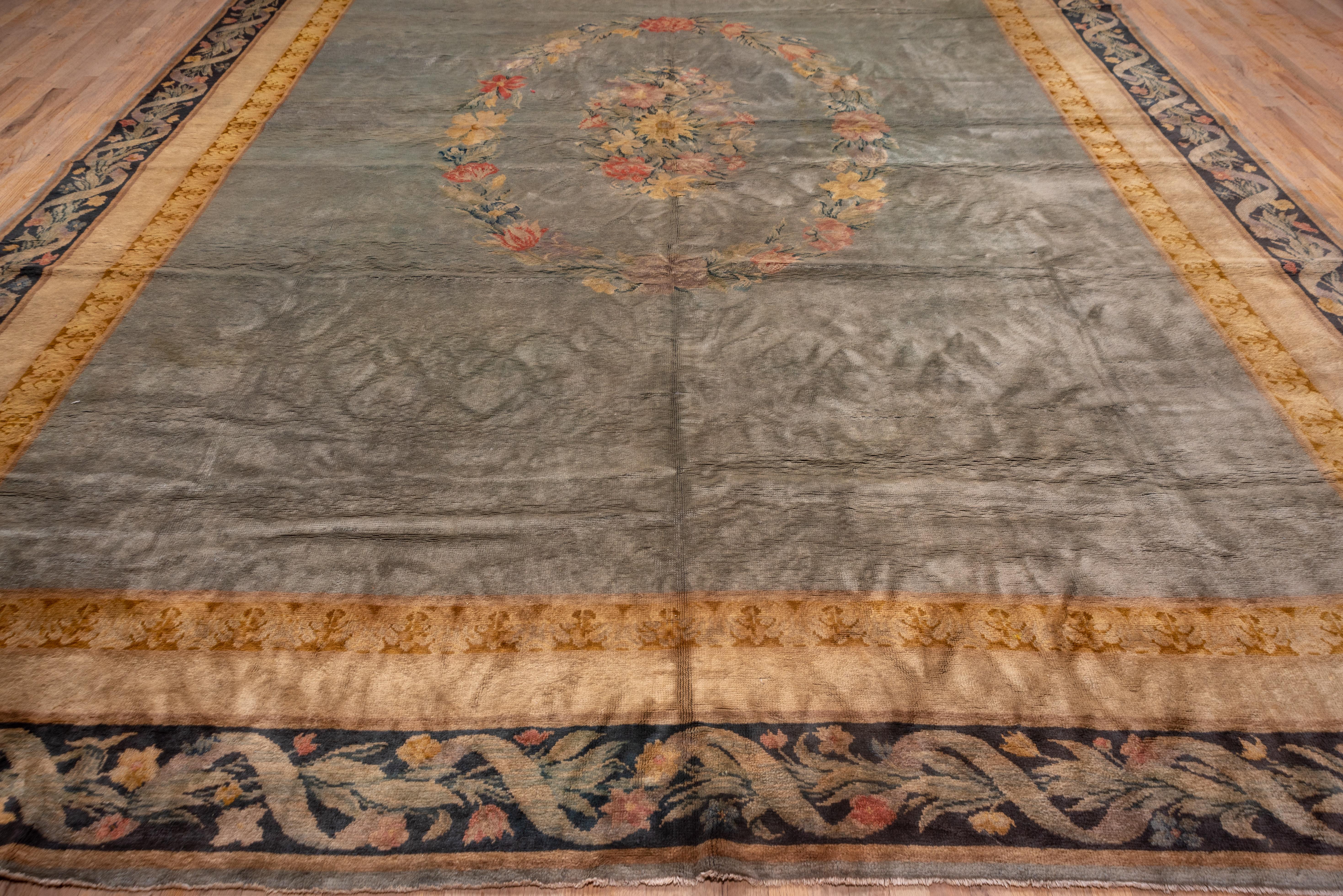 This thick pile, excellent condition French urban carpet features a ribbon and flower border with corner calyxes, framing a light green field with a central leaf and flower wreath surrounding a central bouquet. The field is otherwise unornamented.