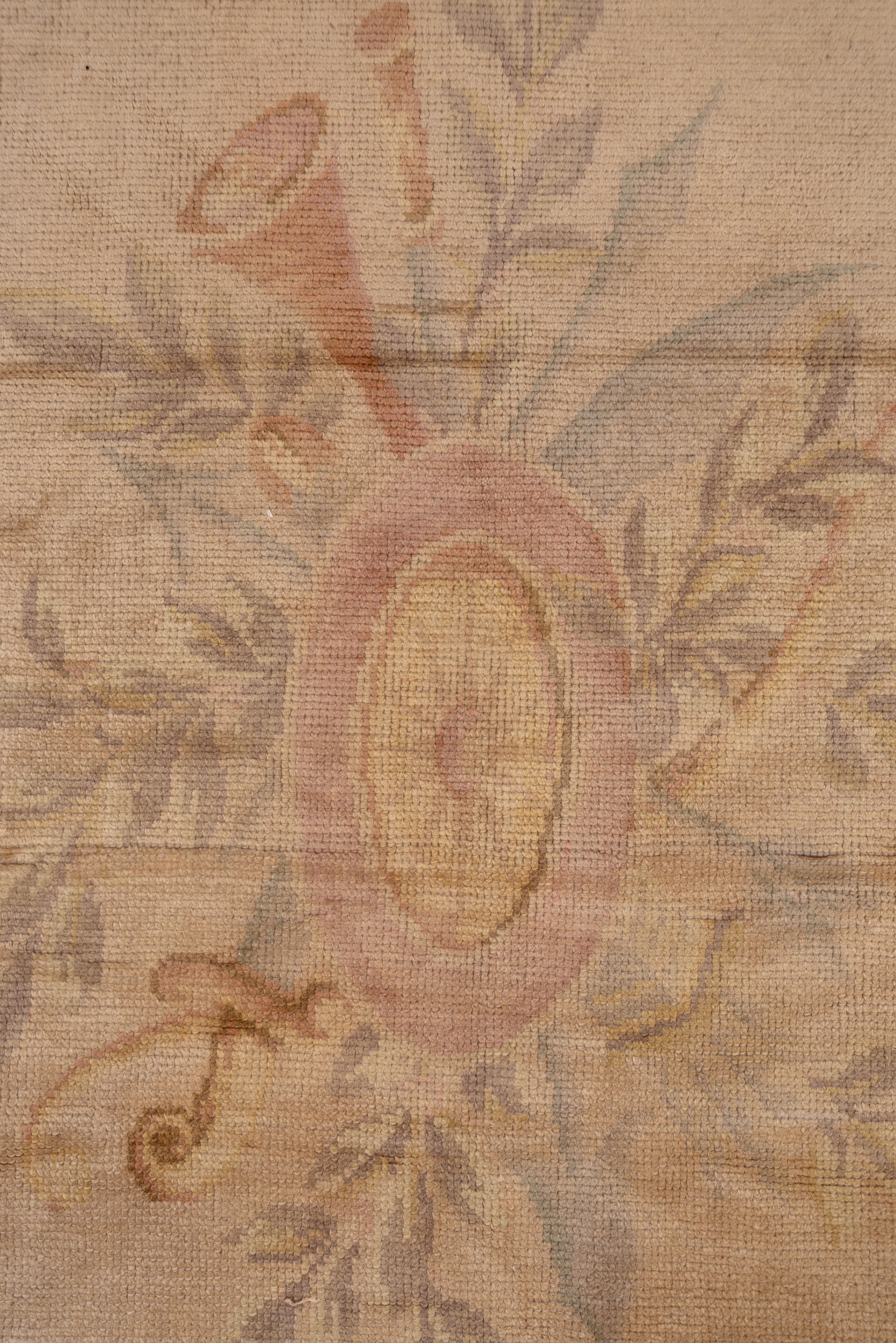 In a French Rococo style, the eggshell field is pointed at one end and shaped by oblique corners and a re-entrant half-cartouche. Small oval medallion with pale straw sub-medallion and mauve-pink border with grasses and flowers. Coarse weave, thick