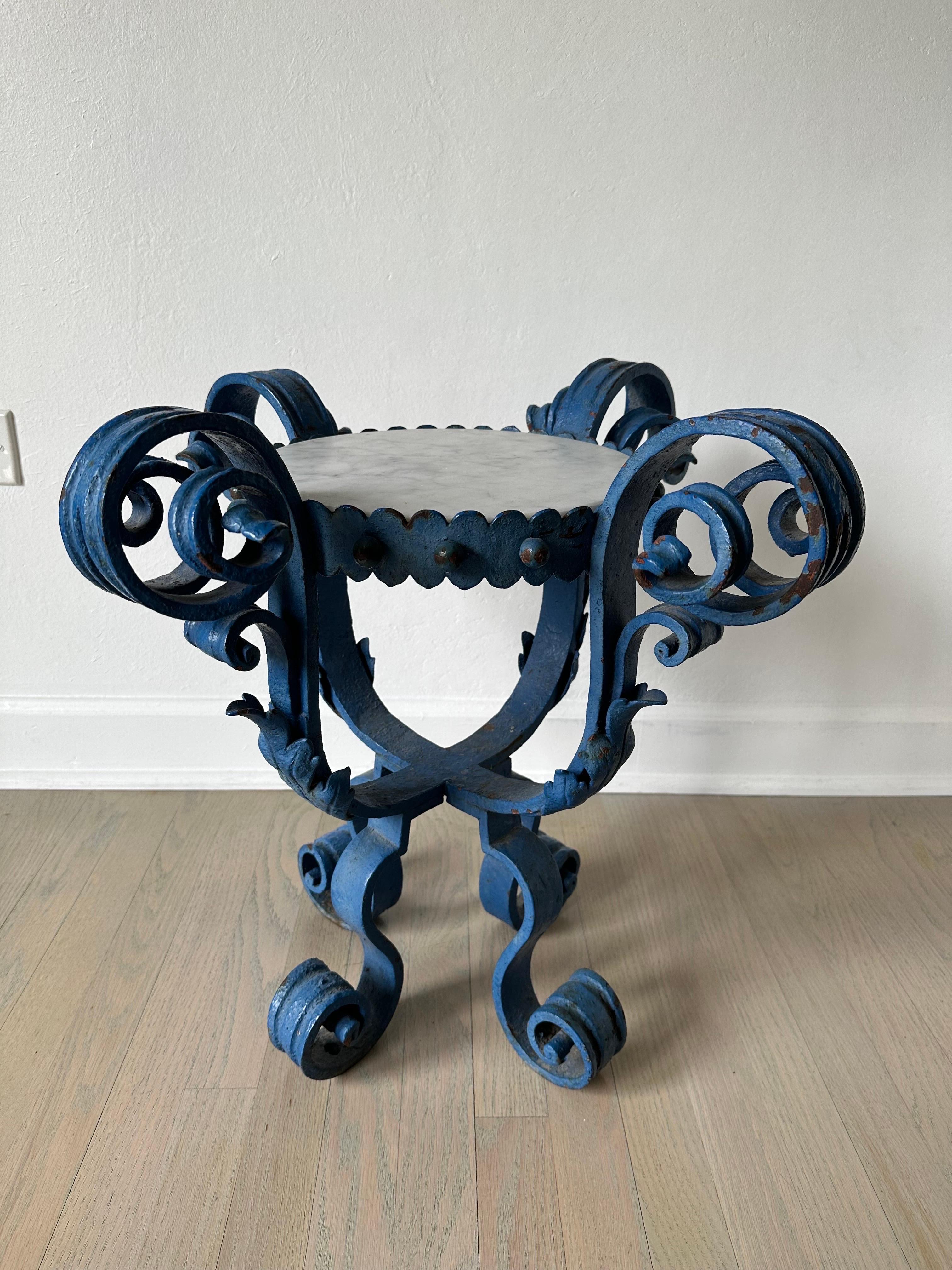 Il s'agit d'une superbe table d'appoint en fer à volutes peinte en bleu. Le plateau est en marbre de Carrare, les accents et les pieds sont en forme de volutes exagérées. Des signes d'âge, de patine et une certaine oxydation sont visibles. Lourd et