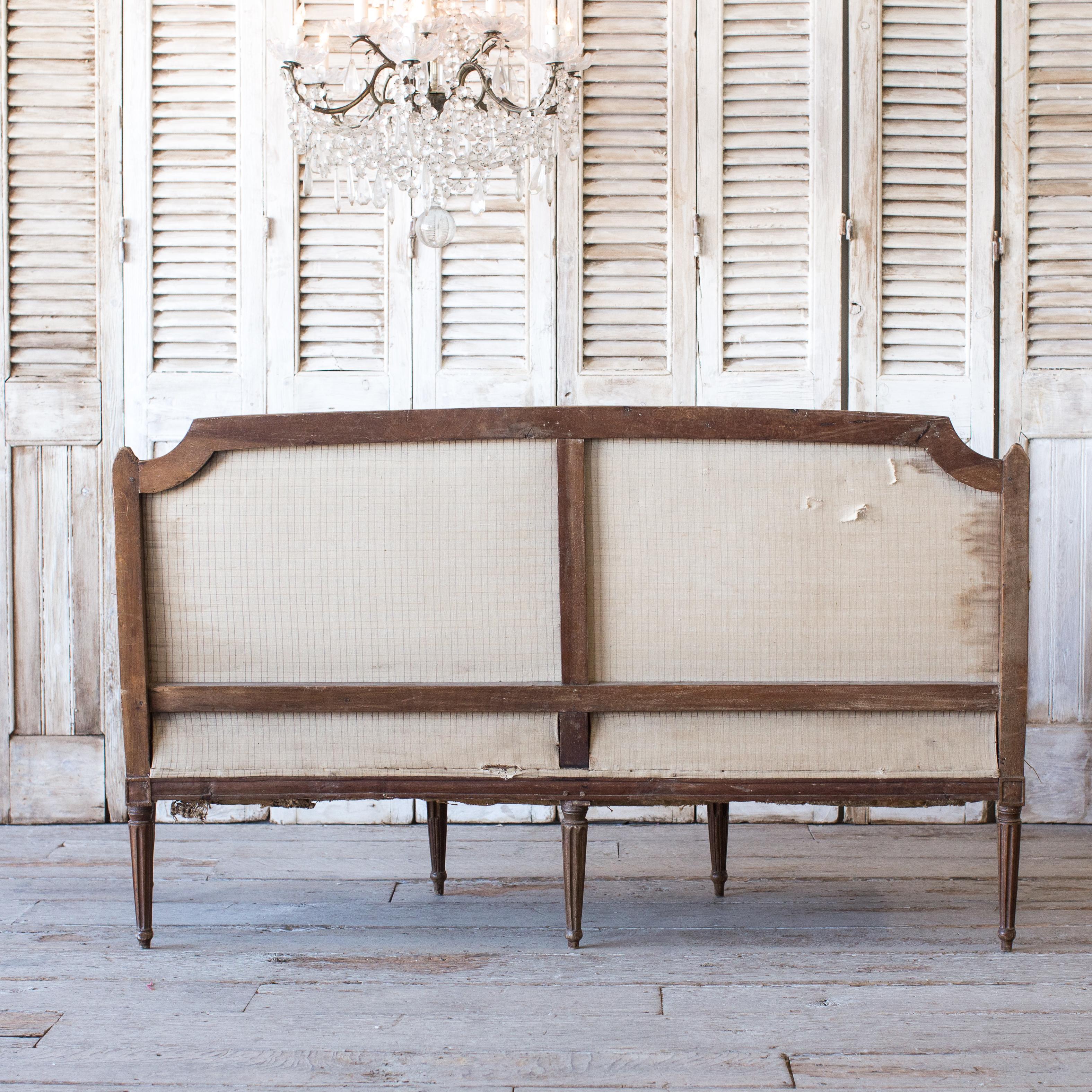 Handsome antique settee sourced in France. This piece boasts a deep brown stain finish with deconstructed cloth. The original muslin underneath and burlap sides give this finely carved frame a rugged feel.