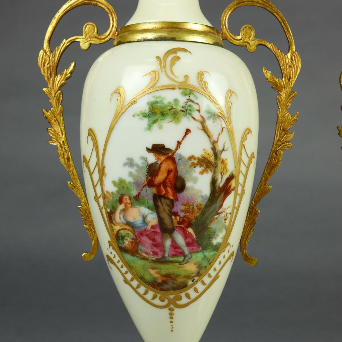 An antique pair of French Sevres School pictorial porcelain urns offer hourglass form each with hand painted reserves of a courting couple flanked by cast bronze scroll and foliate form handles, seated on bronze base and having acorn form cast