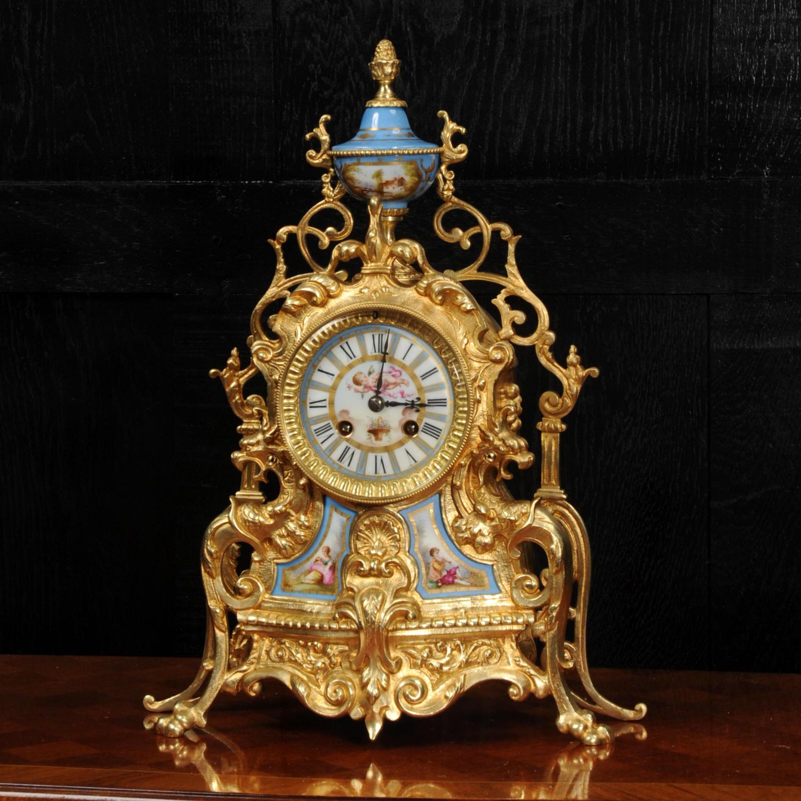 A beautiful antique French gilt bronze clock with exquisitely decorated Sèrves style porcelain panels, urn and dial. It is Baroque in style with scrolling foliage and mythical creatures. The pair of panels show a charming scene of a young gentleman