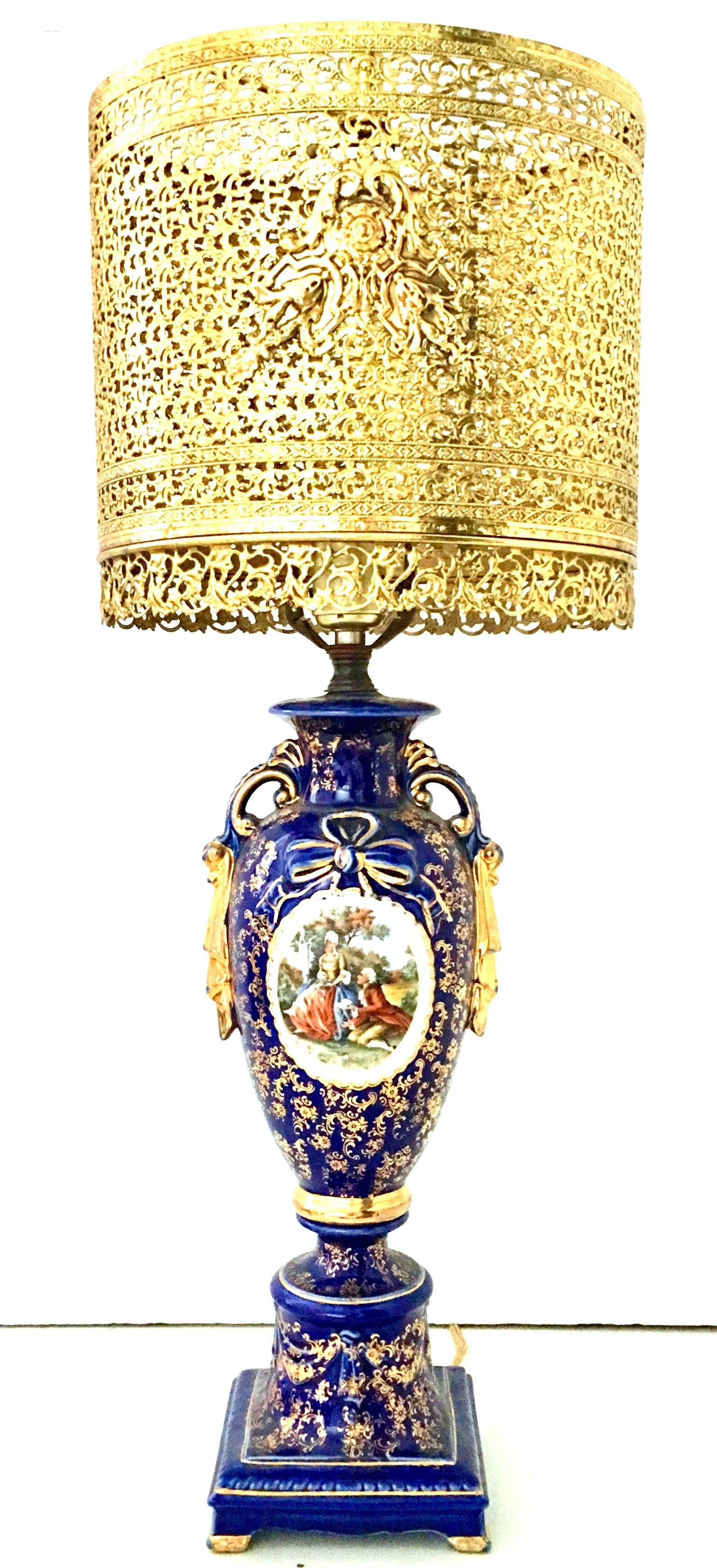 Antique European Sèvres style porcelain cobalt and 22K gilt gold hand-painted Courting couple portrait scene vase lamp. Paired with an Italian gold gilt brass pierced shade. This dramatic and opulent cobalt urn vase form table lamp has a floral and
