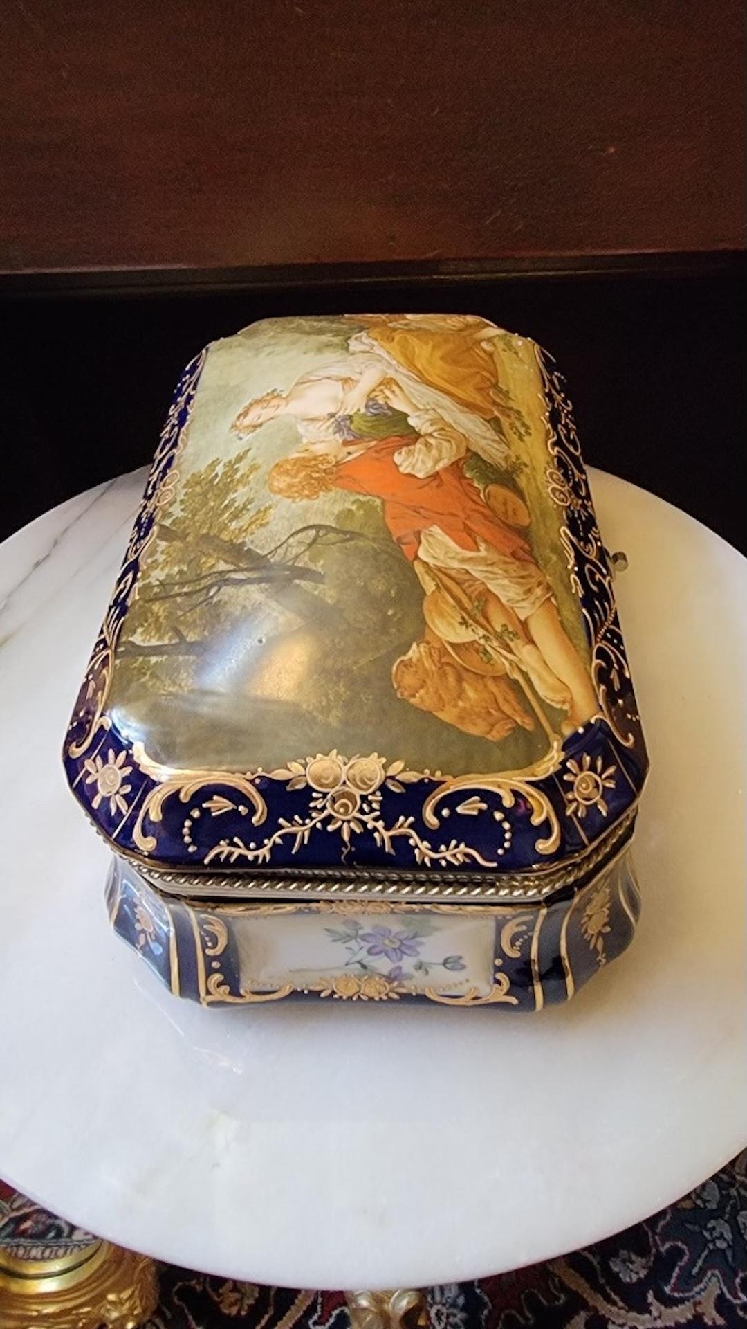 Antique French Sèvres, scatola in porcellana dipinta e ottone dorato

Questo antico portagioie è realizzato nello stile di Sèvres, in Francia, intorno al 1870. Il cofanetto in porcellana ha un bordo blu cobalto e dorato. È dotato di cerniere in
