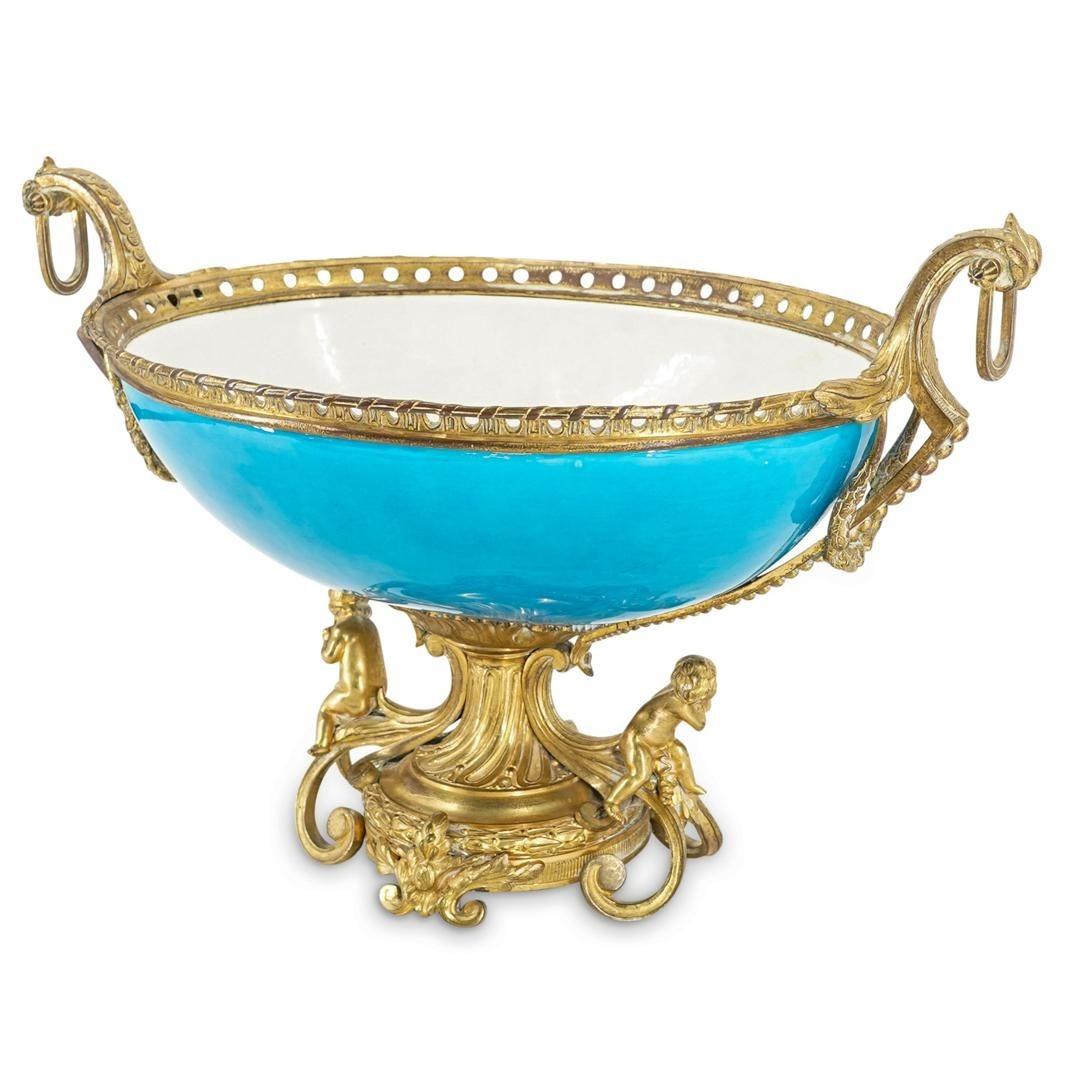 Coupe de centre de table en porcelaine du 19e siècle, de forme ovale, à glaçure bleu turquoise et montures en bronze doré, dont des poignées figuratives représentant des chérubins.  Non signée.