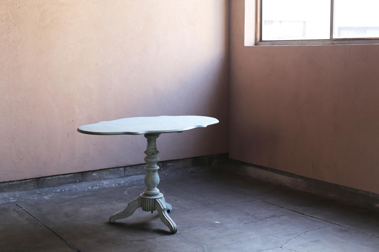 Questo tavolo con piedistallo francese del XIX secolo è rifinito con una morbida vernice grigio-blu, che è invecchiata fino a diventare più tenue. 
Il piano del tavolo con i suoi bordi ondulati, la gamba centrale elegantemente tornita e la base a