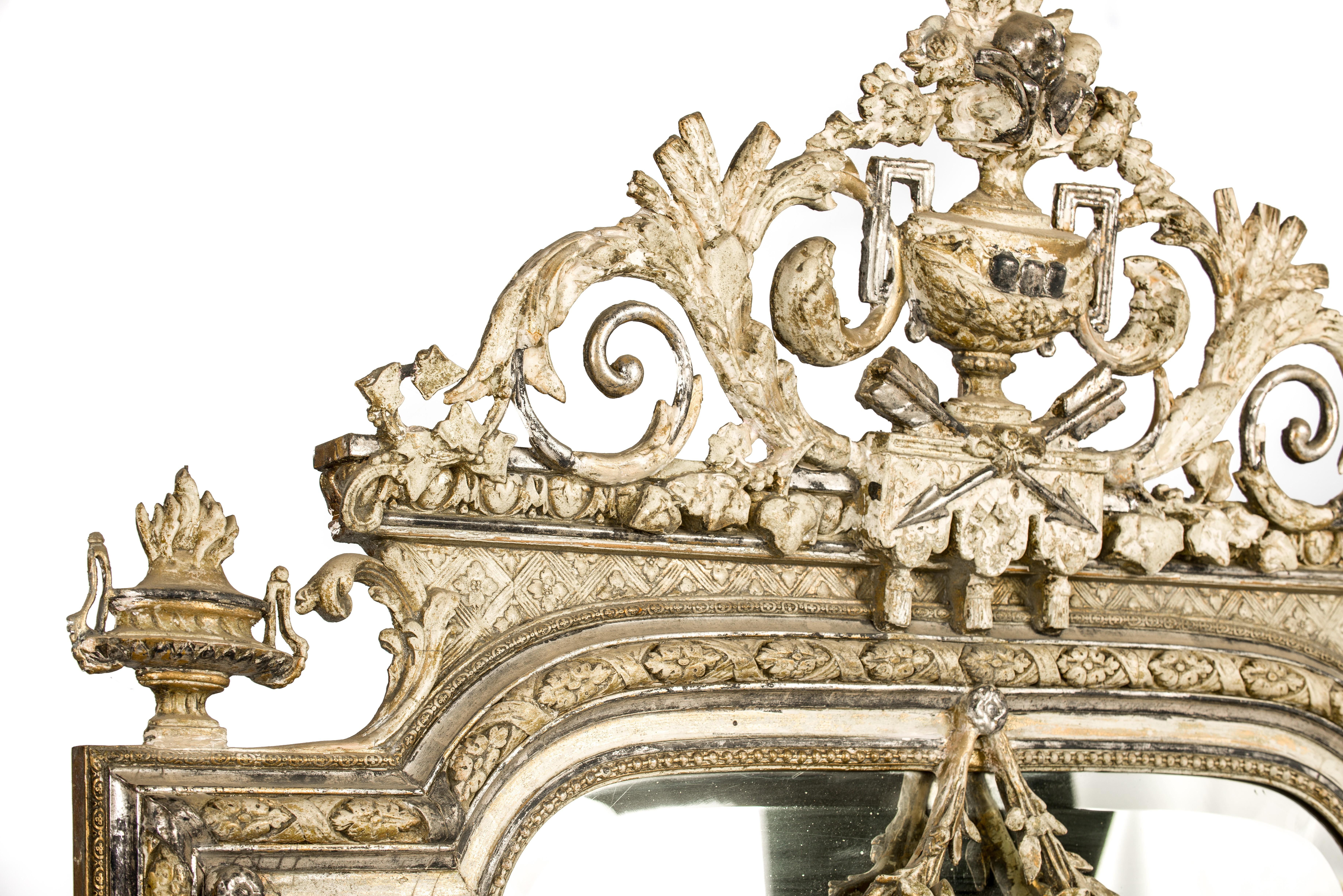 Un miroir Louis XVI impressionnant et richement décoré qui a été fabriqué dans le nord de la France en 1905. 
Le cadre du miroir a été fabriqué en pin massif, a un sommet en arc de cercle et a été décoré avec des ornements moulés. Le cimier orné