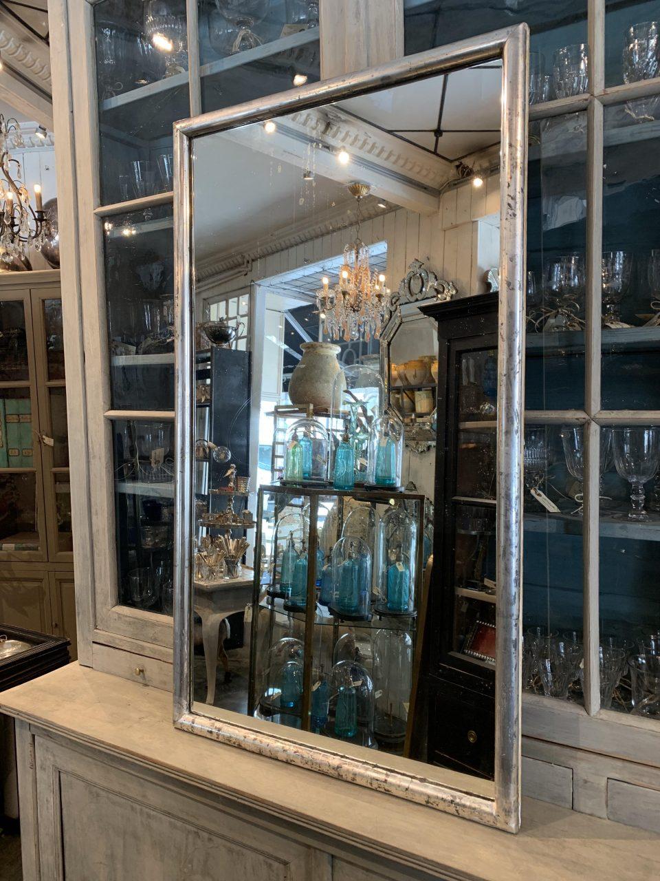 Large and handsome antique French mirror from around 1880-1890s, surrounded by a charming sleek rounded and patinated silver frame. The mirror still retains the original fine silver leaf coating on the frame and the old mercury mirror