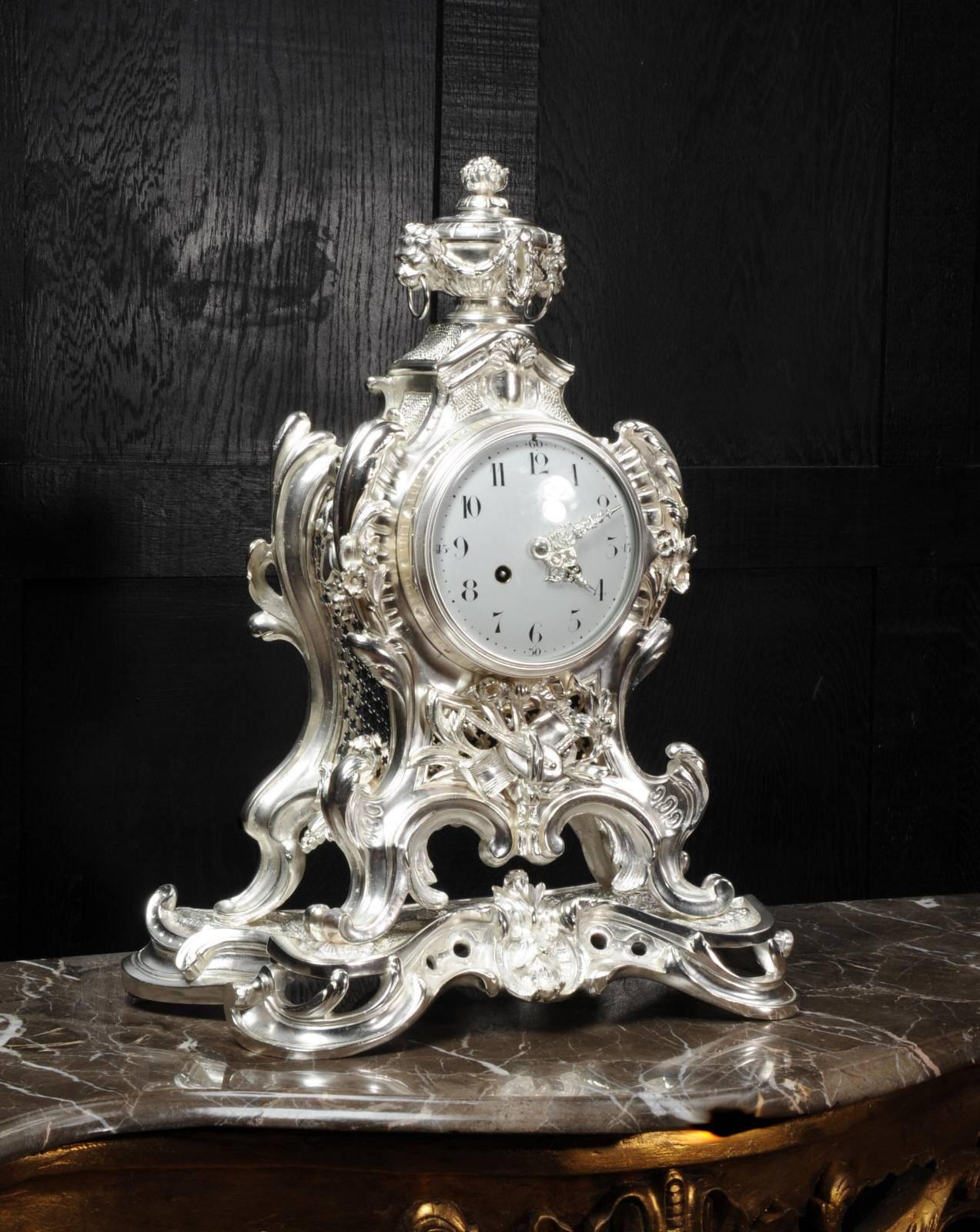 A rare and spectacular antique French Rococo clock of large proportions C1880. Formed of silver plated bronze with bold sweeping curves and floral swags and standing on a large naturalistically modelled base. Below the dial is a collection of