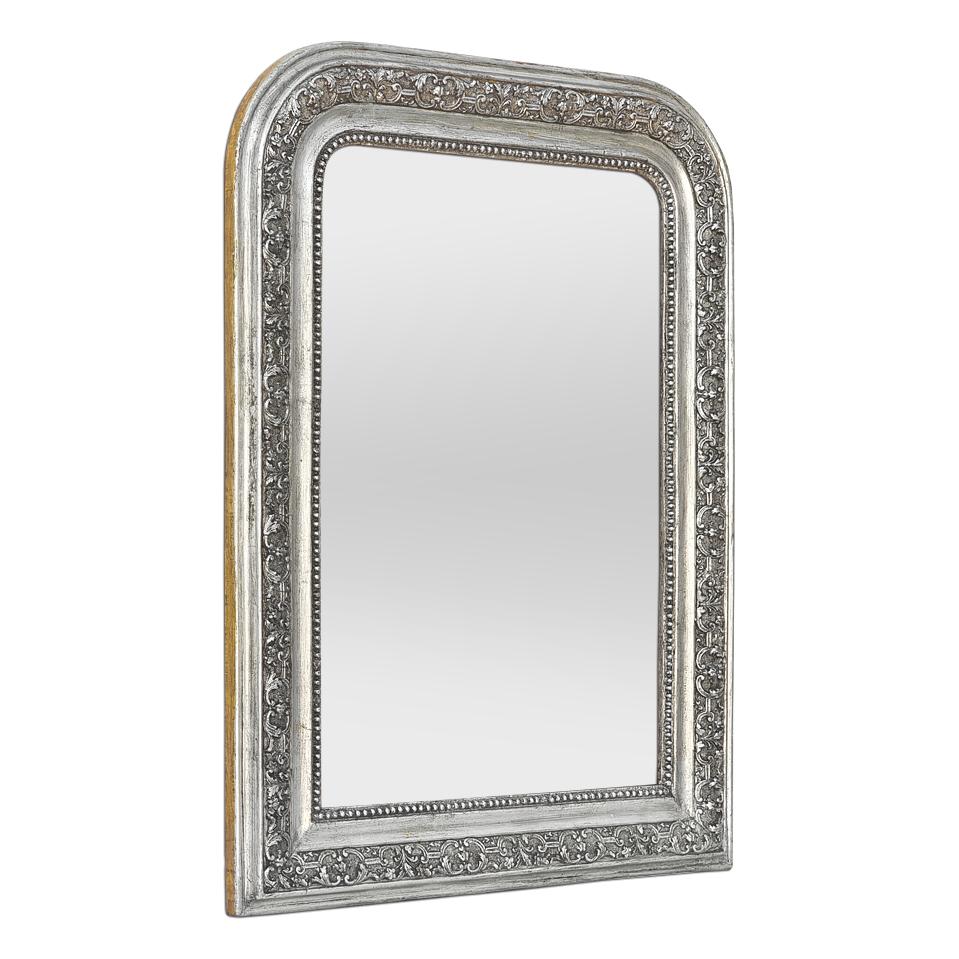 Miroir mural ancien de style Louis-Philippe en bois argenté patiné, vers 1900. Inspirées de l'Art nouveau, les décorations comportent des rinceaux de feuillage et de fleurs, ainsi qu'une guirlande de perles sur le pourtour du miroir en verre. Cadre