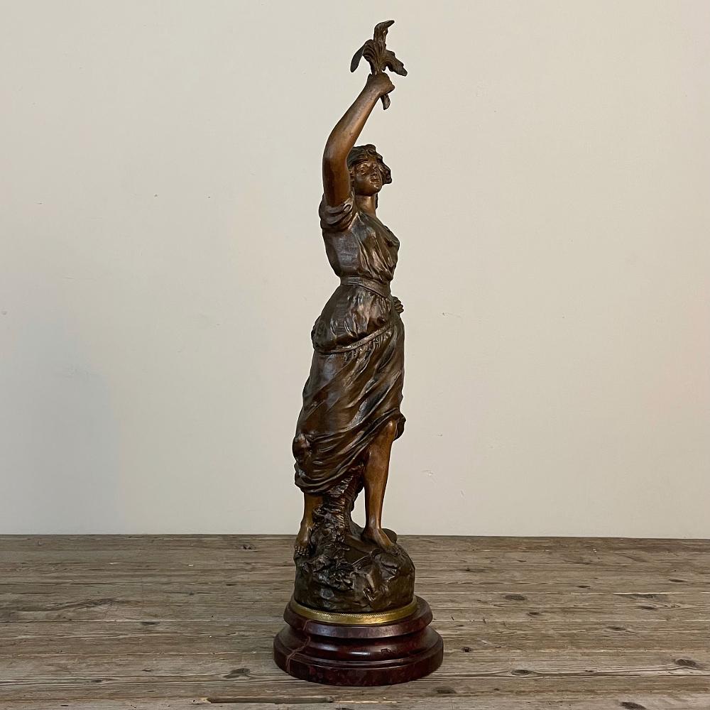 Antique French spelter statue of Maiden by Rullony was created during the early years of the Art Deco Period, with the beautiful subject in a classical pose holding tobacco leaves above her head. Attractive young women frequently appeared in markets
