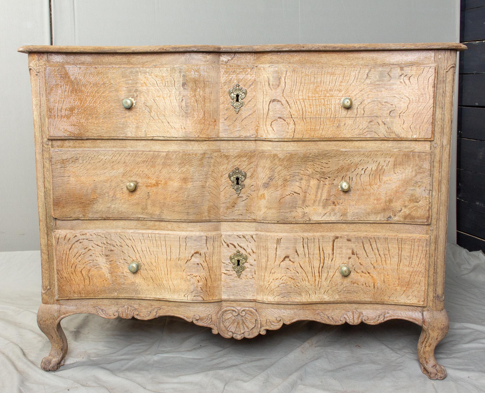 This is an antique French oak commode featuring curved-front drawer with brass pulls and escutcheons. There are three drawers which are on rails, and each opens and closes smoothly. There is some fluting on the corners and the top is finished with a