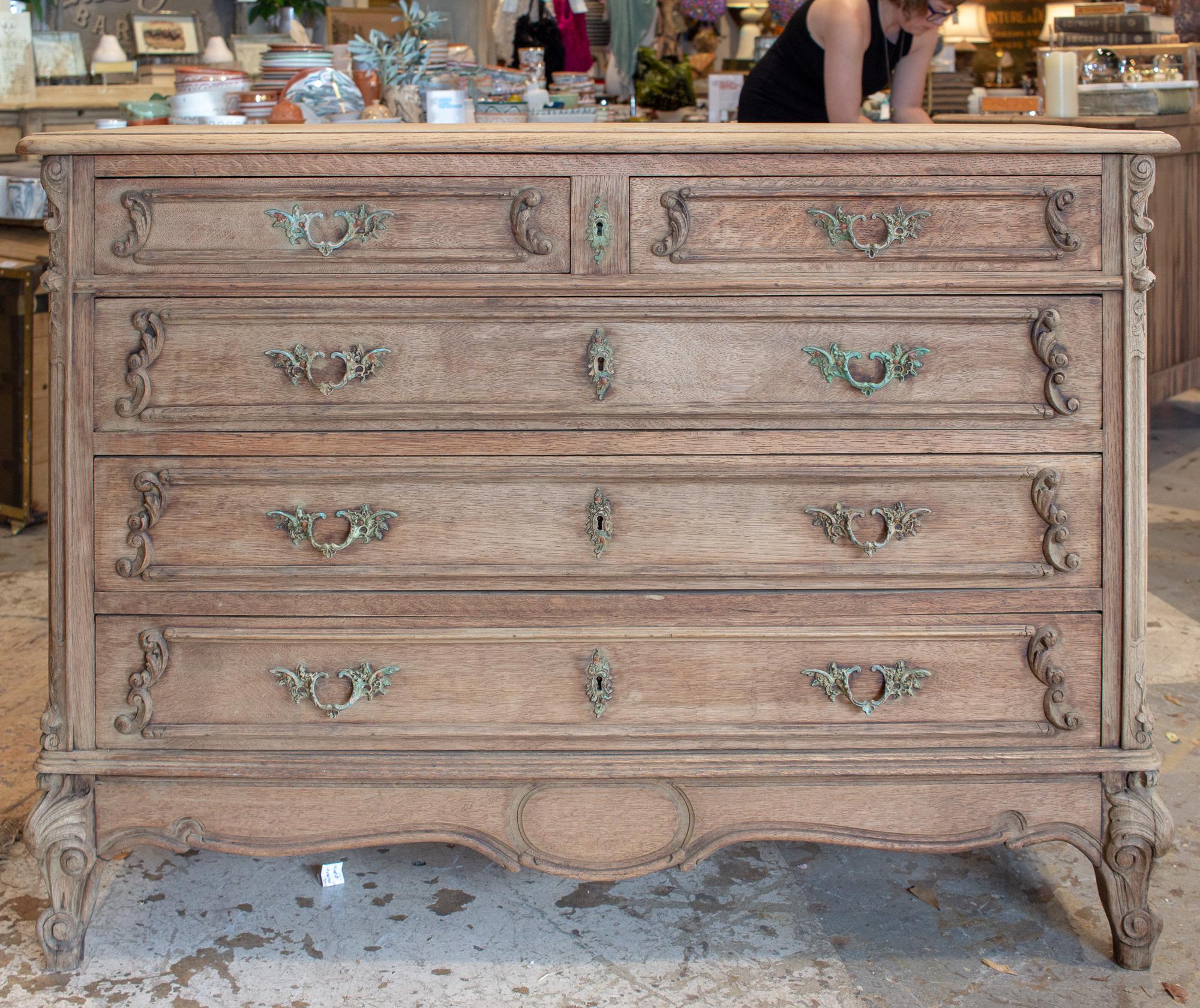 This antique commode was sourced in France and features five drawers and beautifully detailed carvings accented by wonderfully patinated hardware. The drawer fronts feature fantastic scroll work along with metal handles and escutcheons that have