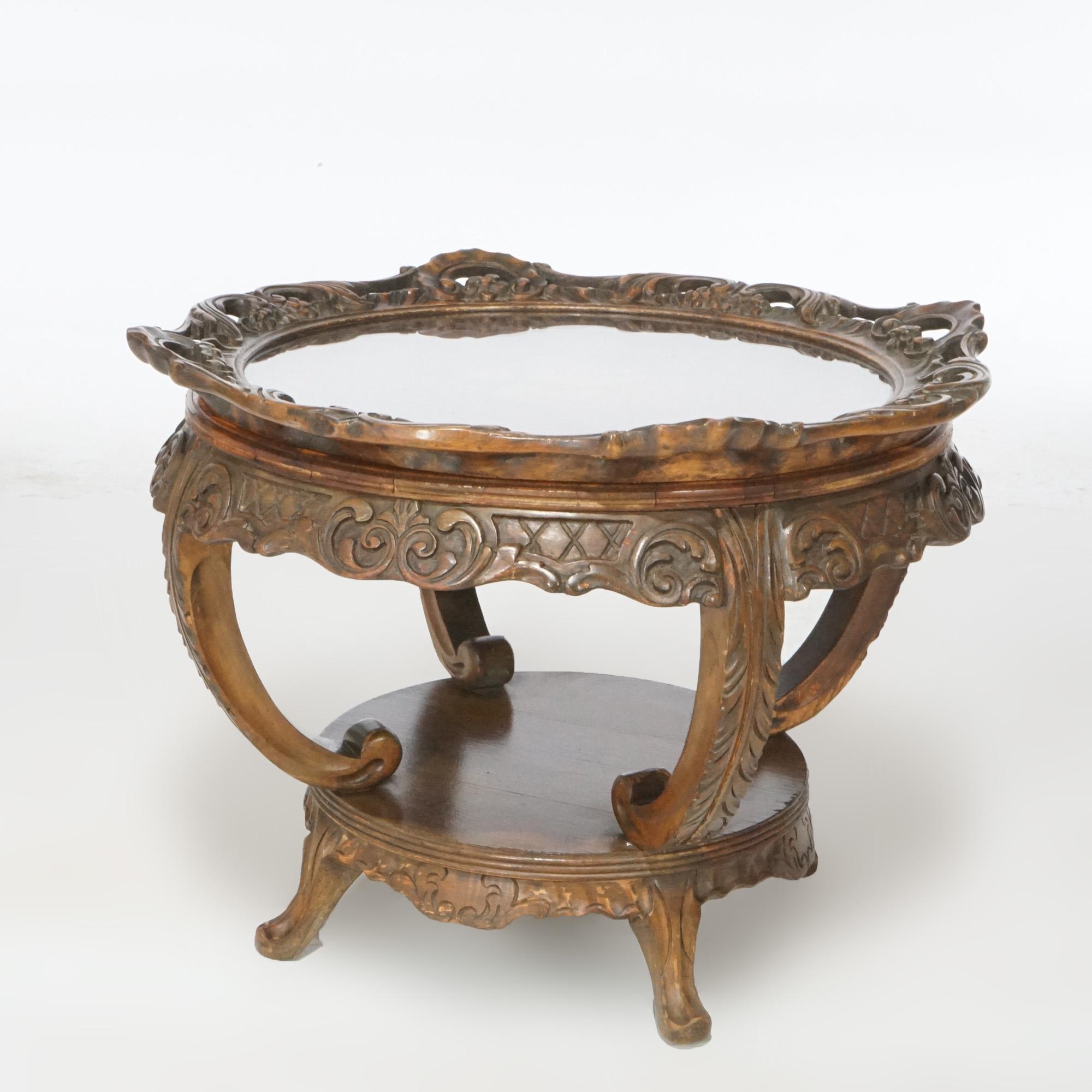 An antique French style side table offers bookmatched satinwood top with central floral marquetry inlay and glass tray having carved foliate border over lazy Susan base raised on scroll form legs with carved acanthus and foliate elements,
