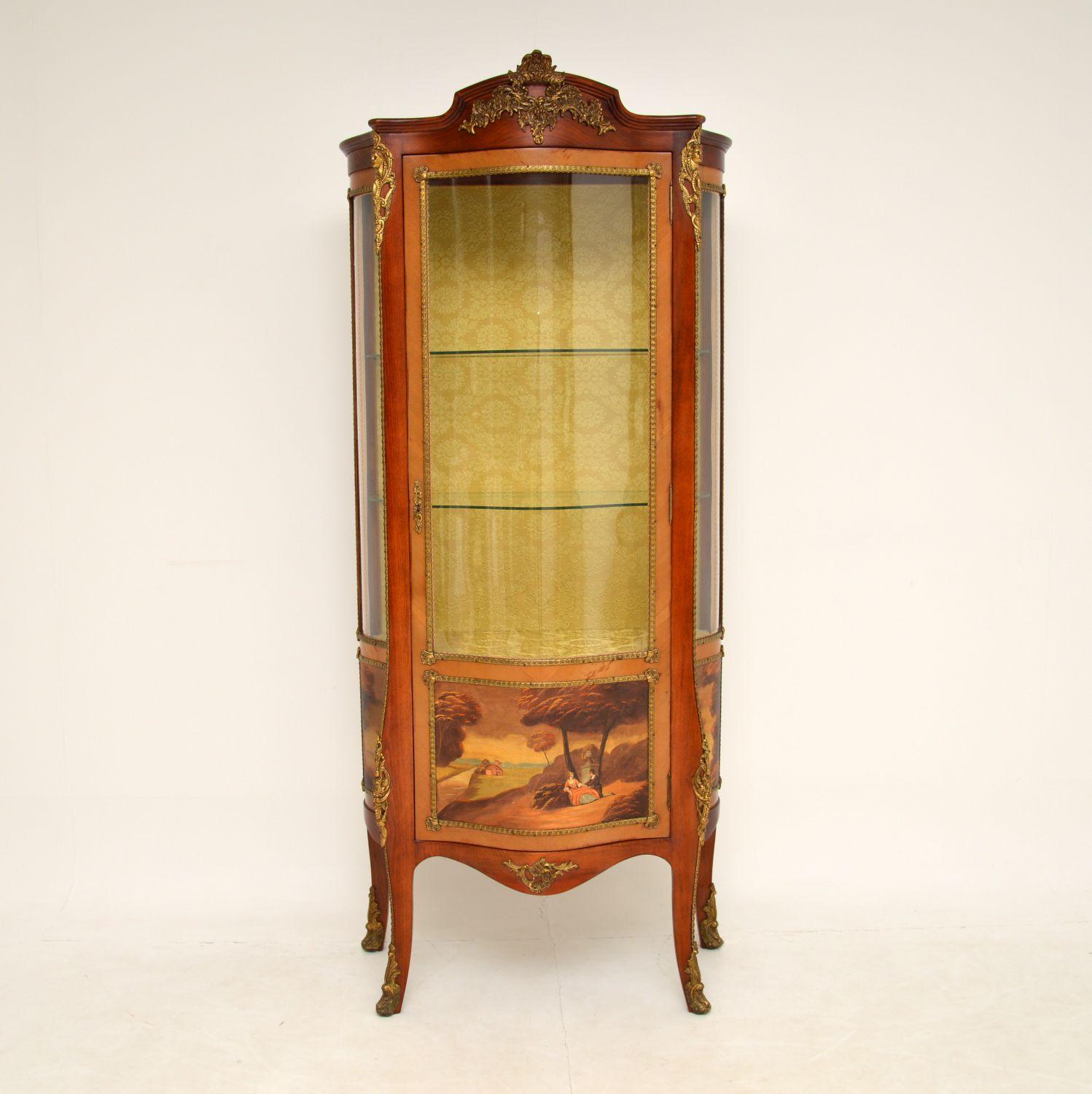 A stunning antique French style display cabinet with a serpentine glass front. This cabinet has the Epstein label inside & it dates from around the 1930’s period.

The quality is fantastic, with gorgeous gilt bronze mounts and beautiful painted