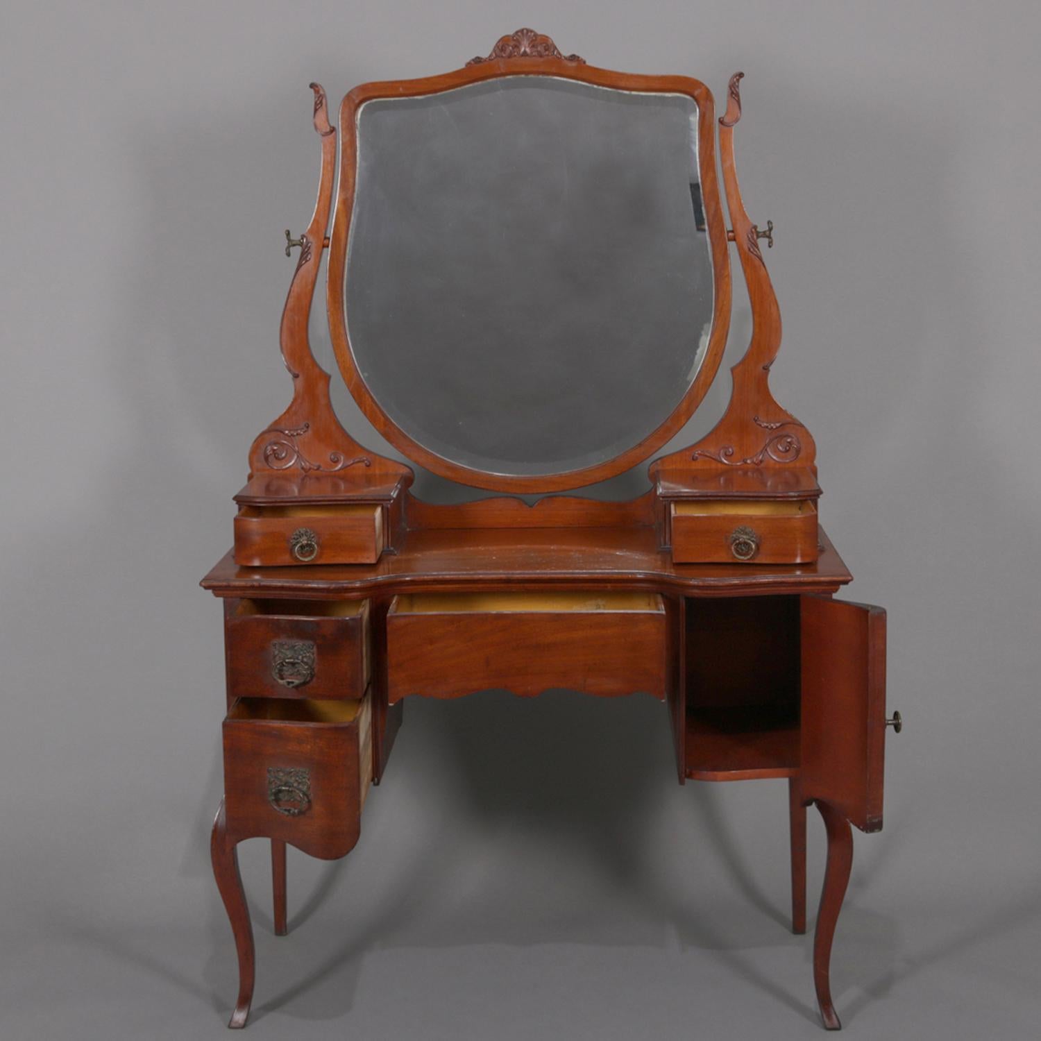 An antique French style dressing table features shield form mirror seated in supports with carved foliate ears, surmounting table with upper glove boxes over case with central frieze drawer, two drawers and single side cabinet, raised on cabriole