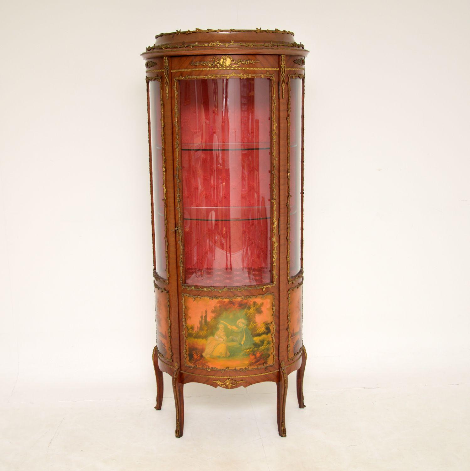 A stunning painted and ormolu mounted antique French style display cabinet, which we would date from around the 1930’s period.
It is of lovely quality, with a finely made curved glass front and sides. The wood has stunning gilt bronze mounts all