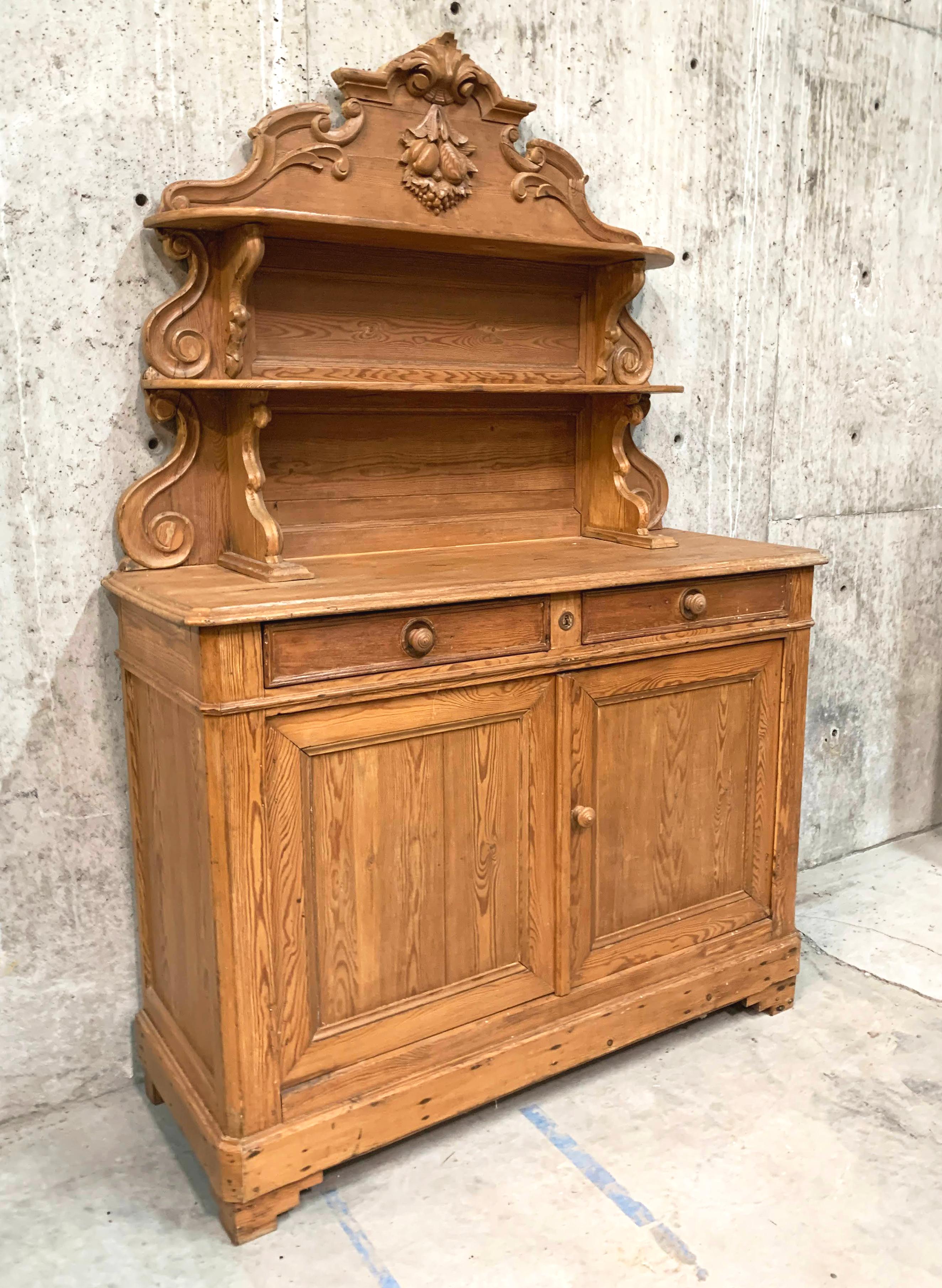This Louis Philippe style buffet, in dramatically grained and colored pine, is a versatile and attractive piece of furniture. The unique scrolling upper shelves and exquisitely carved fruit ornamental crown gives this piece real presence. Classic