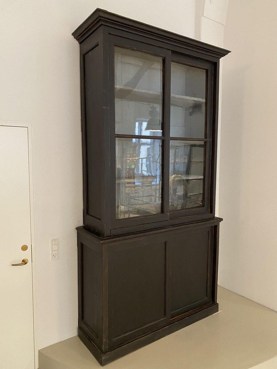 Tall, handsome and well-proportioned antique 2-piece French display cabinet the early 1900s. Imposing large sliding glass doors. Beautifully patinata in a matte black paint and with two tall sliding doors in the upper part of the cabinet, in