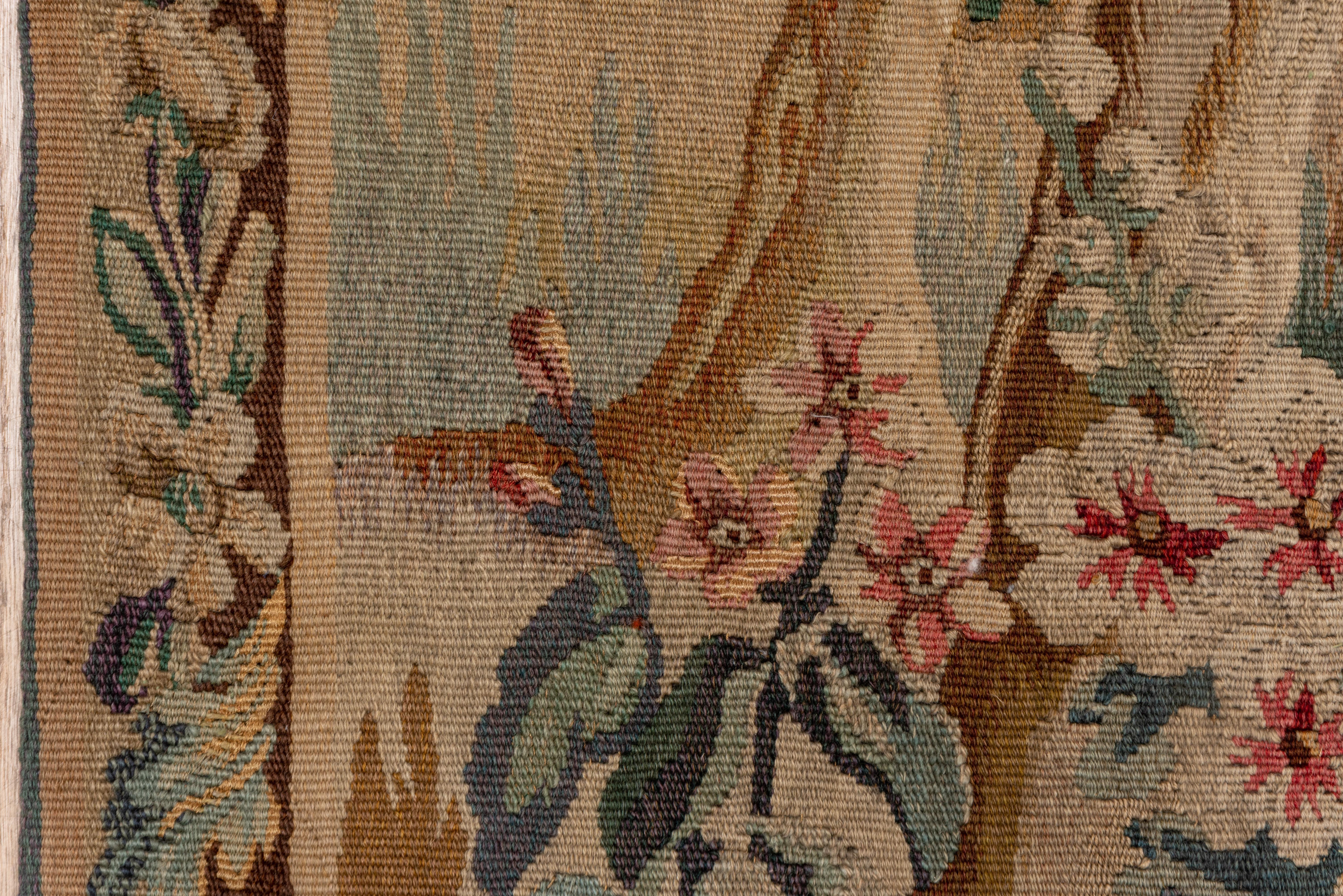 This softly toned verdure tapestry shows two leafy trees framing a scene of a fox and chicken, with a receding rustic landscape behind. Only the animal action disturbs the tranquil summer scene. Red and green rose and leaf border.