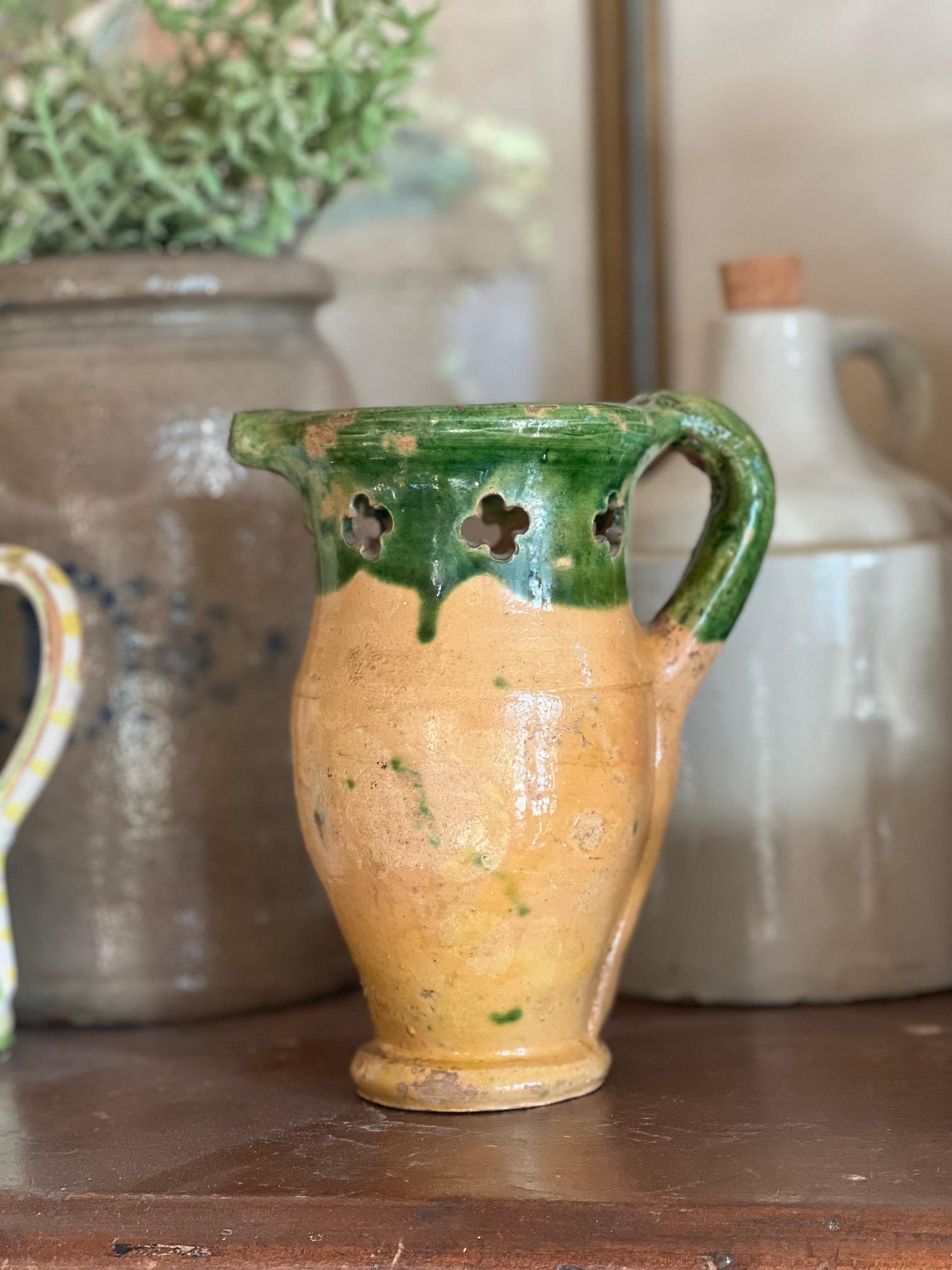 Unique antique French terra cotta vessel with green drip paint on the top. There are seven cut outs at the top, the spout is covered, and it has an applied handle.