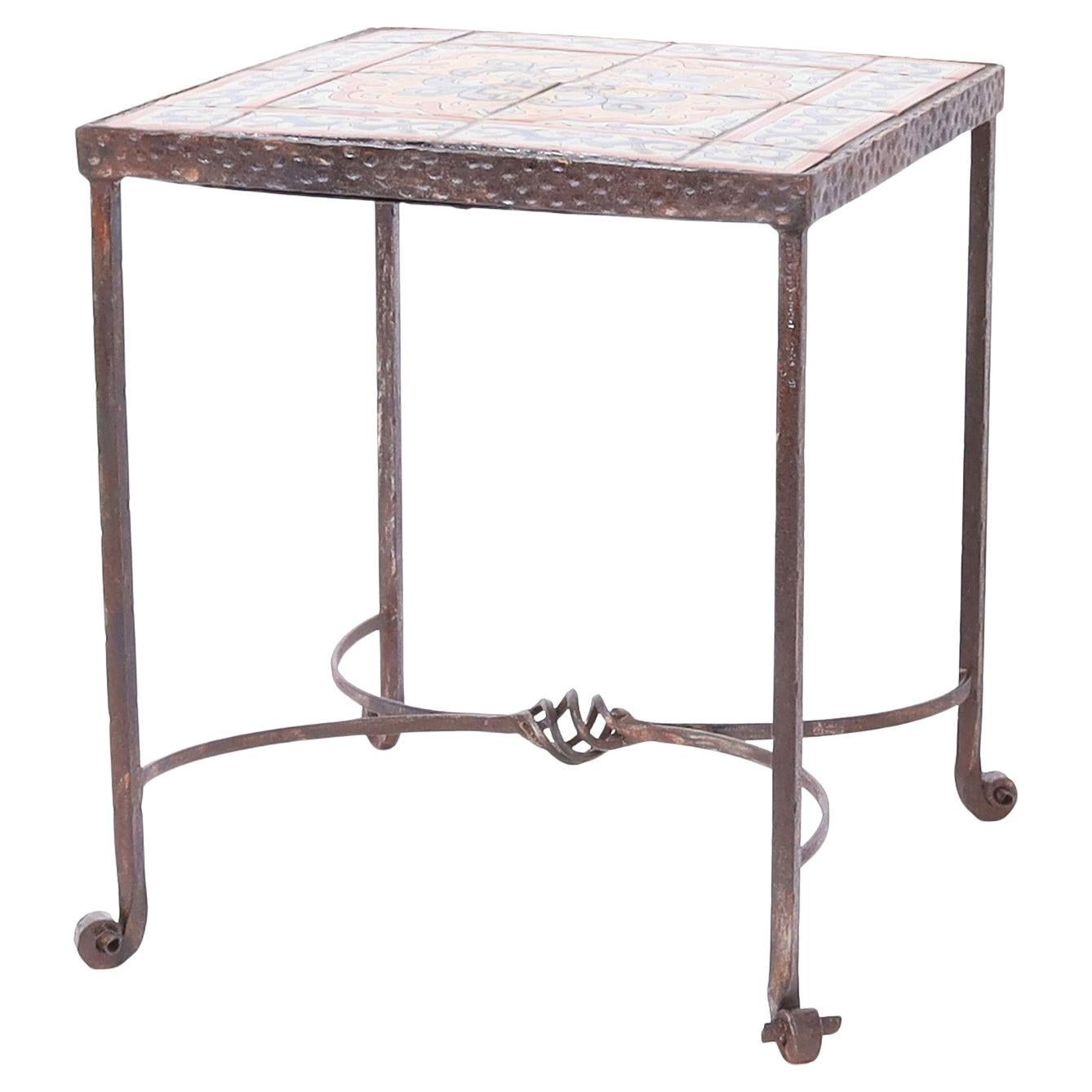 Impressionnante table d'appoint française ancienne avec un dessus carré ayant des carreaux avec des fleurs de lys stylisées dans des couleurs méditerranéennes sur une base travaillée à la main avec des pieds roulés.