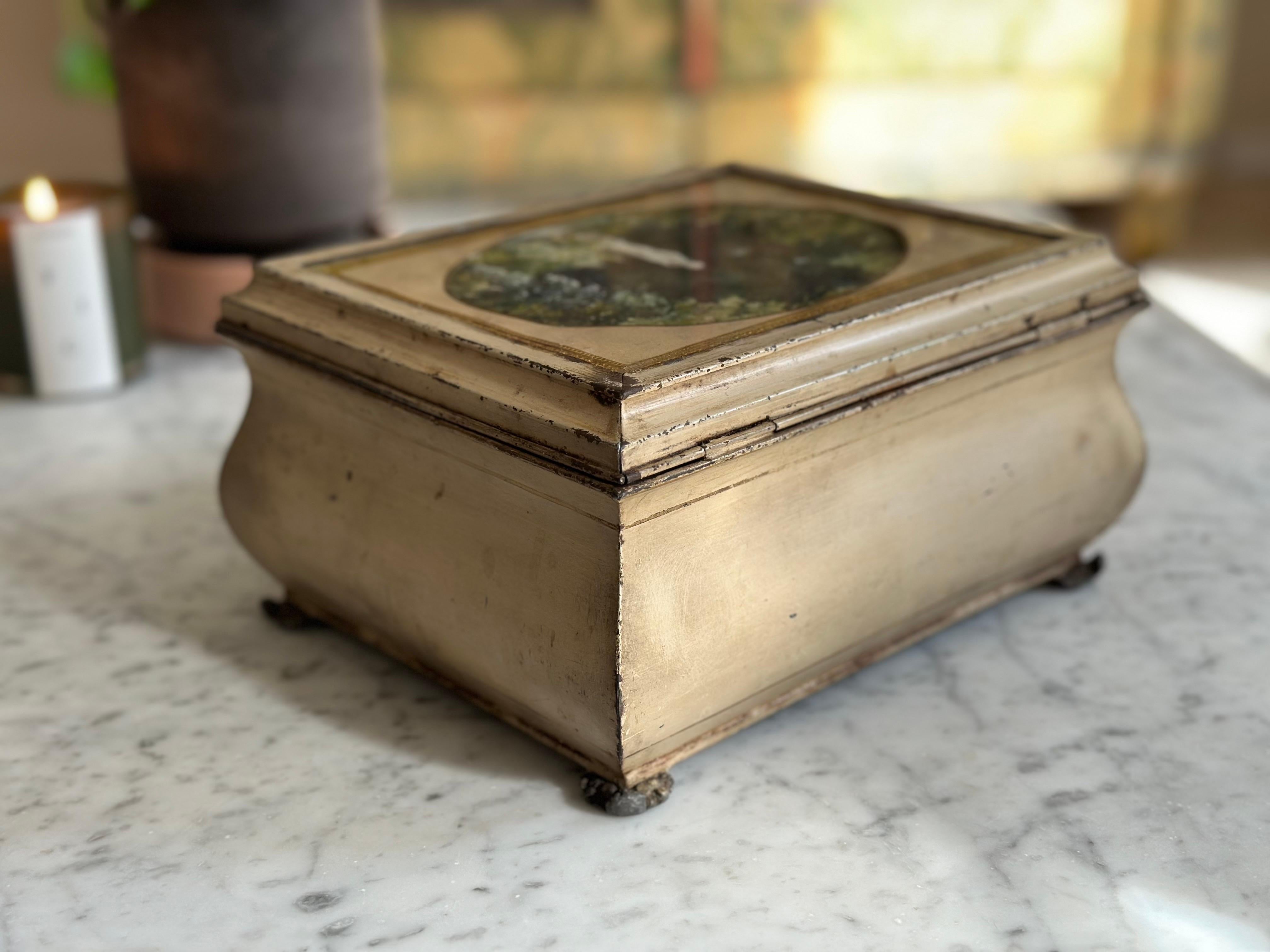 Esta antigua caja de hojalata francesa de hacia 1890 captura la elegancia de la artesanía del siglo XIX con su diseño único y sus encantadores detalles. Con forma de cofre de madera, la caja tiene una forma redondeada y bulbosa, asentada sobre