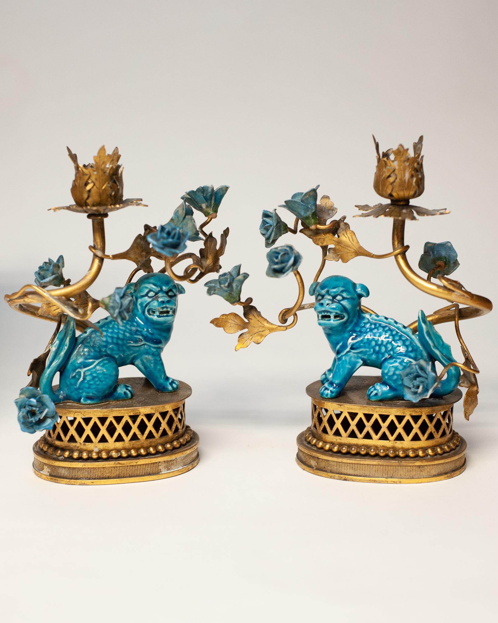 A stunning pair of French antique foo fu dog candlesticks or lamp bases, glazed in a bright turquoise. This pair may be unwired and rewired for use as lamps, or used to hold candles. Porcelain Foo Dogs and porcelain flowers with brass bases, leaves