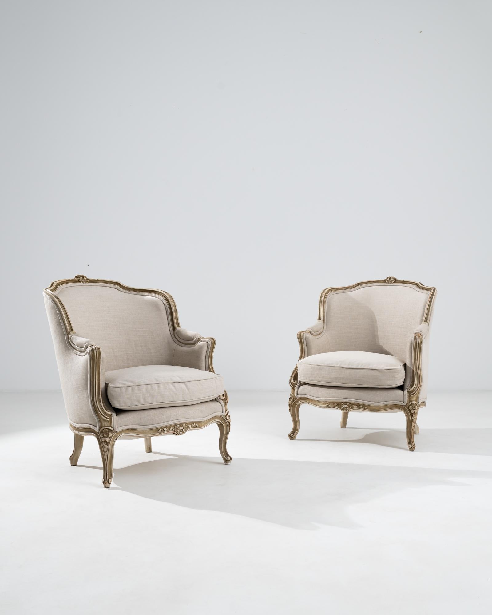 Made in France, circa 1900, this pair of wooden armchairs features a stately profile, with wide seats and upholstery that wraps generously around the chair’s back, reflecting the refined comfort of the French Provincial style. Contoured armrests,