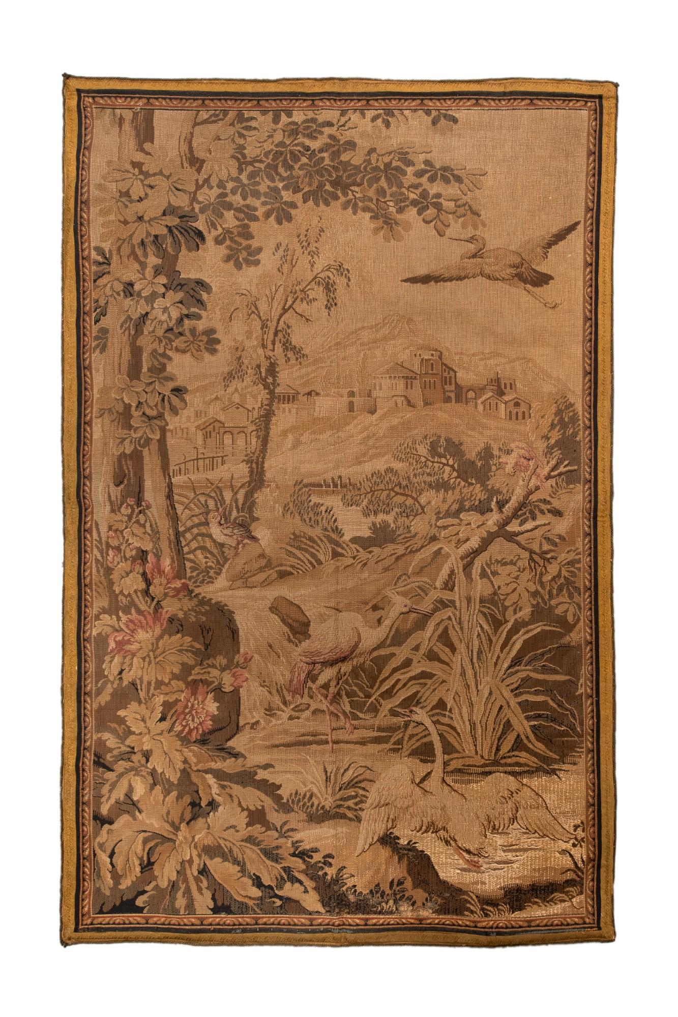 Este elegante tapiz antiguo francés de verdura representa un sereno paisaje pastoral habitado por pájaros de largas patas, exuberante follaje y un lejano pueblo situado sobre ondulantes colinas. Típica de los talleres de Aubusson y Beauvais del