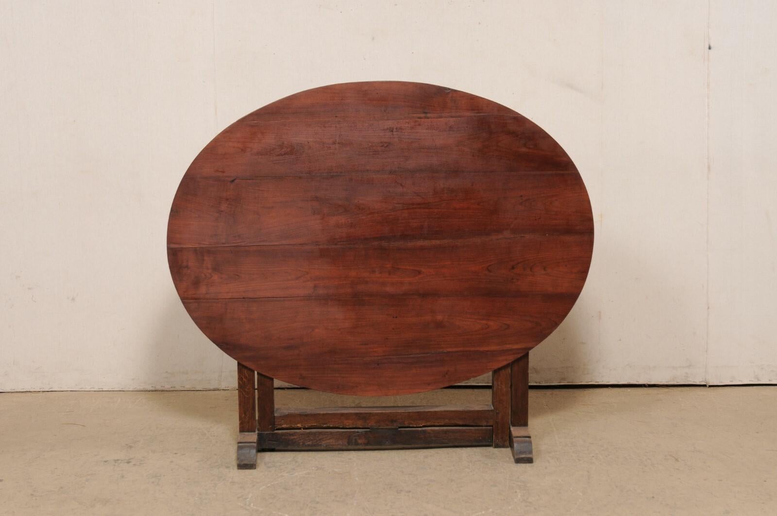 A French tilt-top wooden wine tasting table from the early 20th century. This antique table from France features an oval-shaped tilt top, which was the signature of wine tasting tables during this time. When in use, the top is supported with a boxed