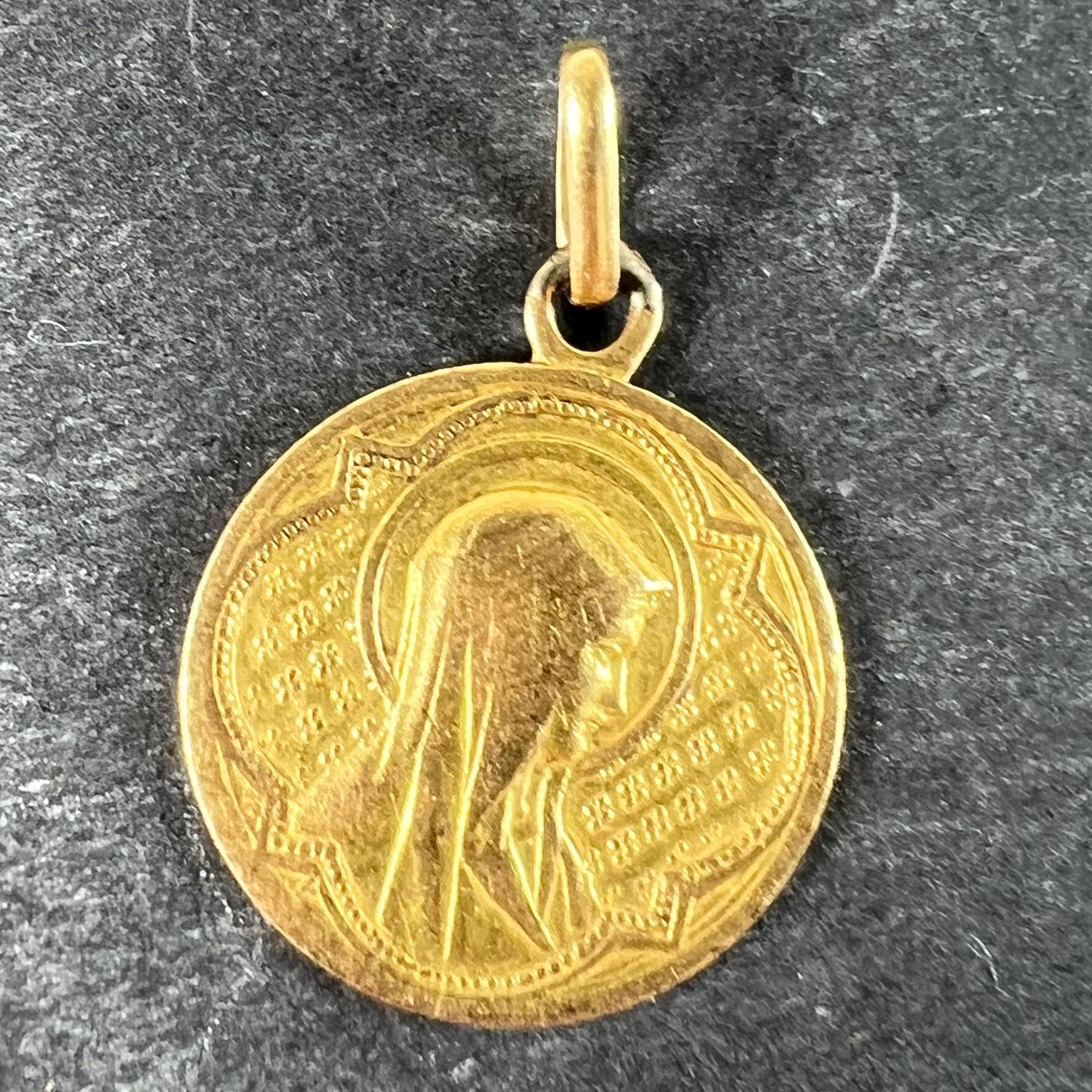 An antique French 18 karat (18K) yellow gold charm pendant designed as a round medal depicting the Virgin Mary within a Gothic frame. The reverse shows a sheaf of lilies with the engraved monogram MB and the date 2nd Juin 1873. Unmarked but tested