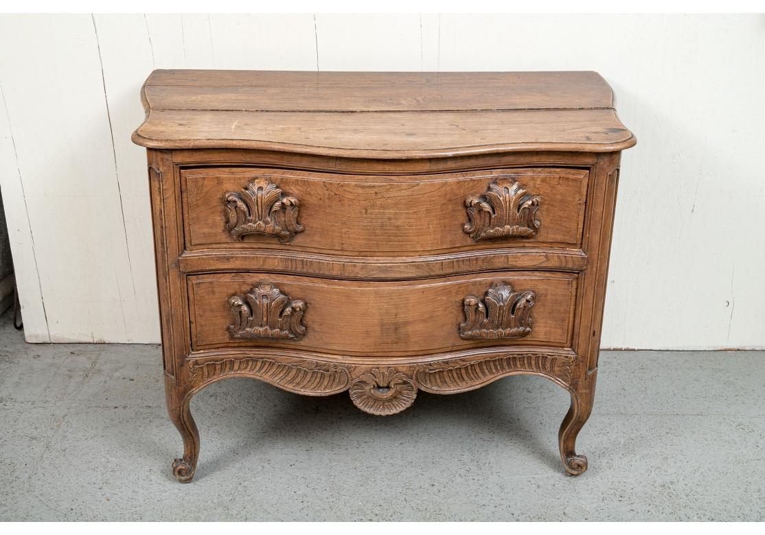 A timeworn and very decorative Antique French Chest with two large drawers and fine traditional carving. French walnut commode with serpentine front, prominent and heavily carved foliate pulls, the bottom with fluted motif with shell, paneled back,